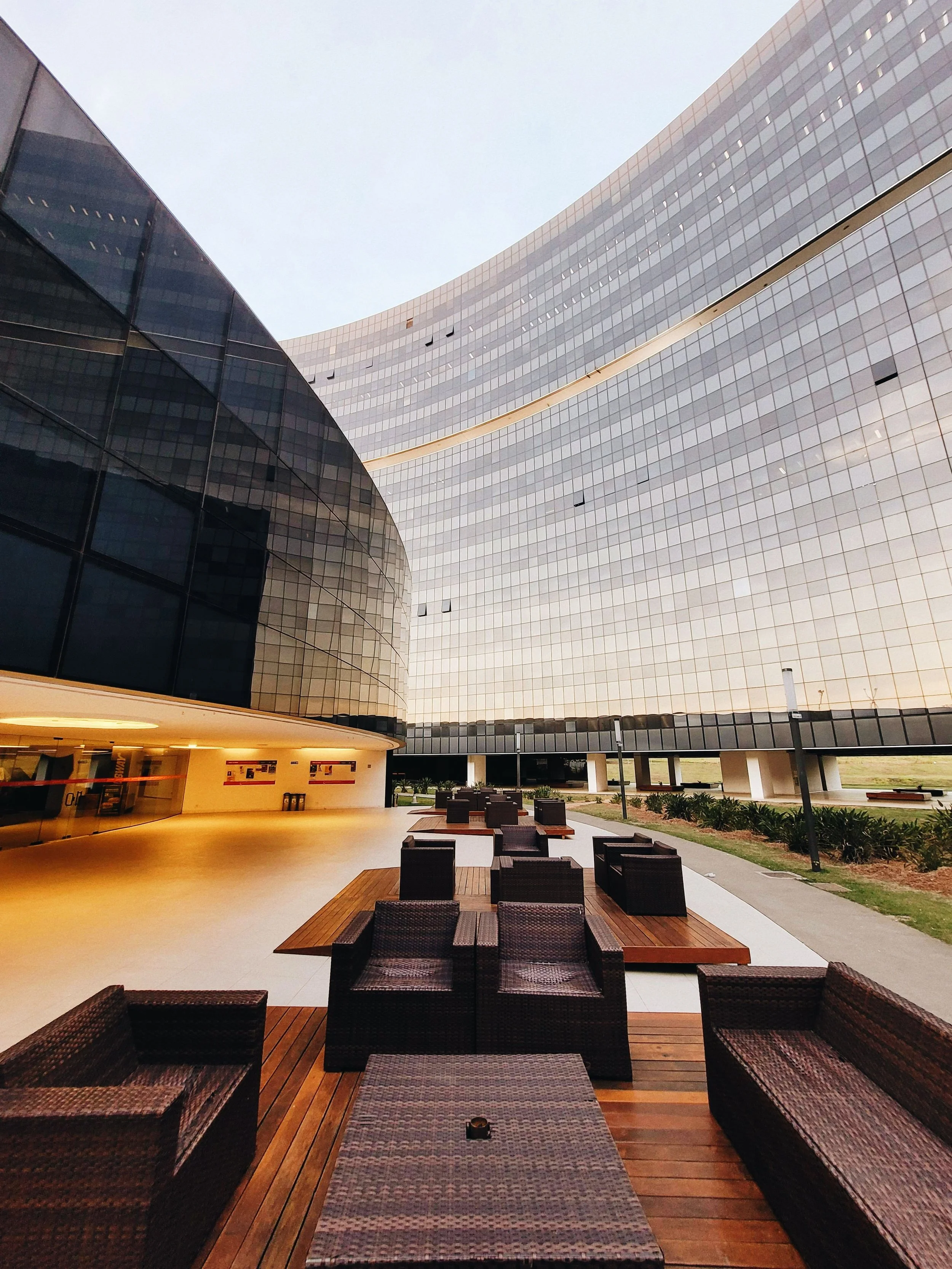 Outdoor patio area with wicker chairs and tables, adjacent to a modern building with reflective glass windows.