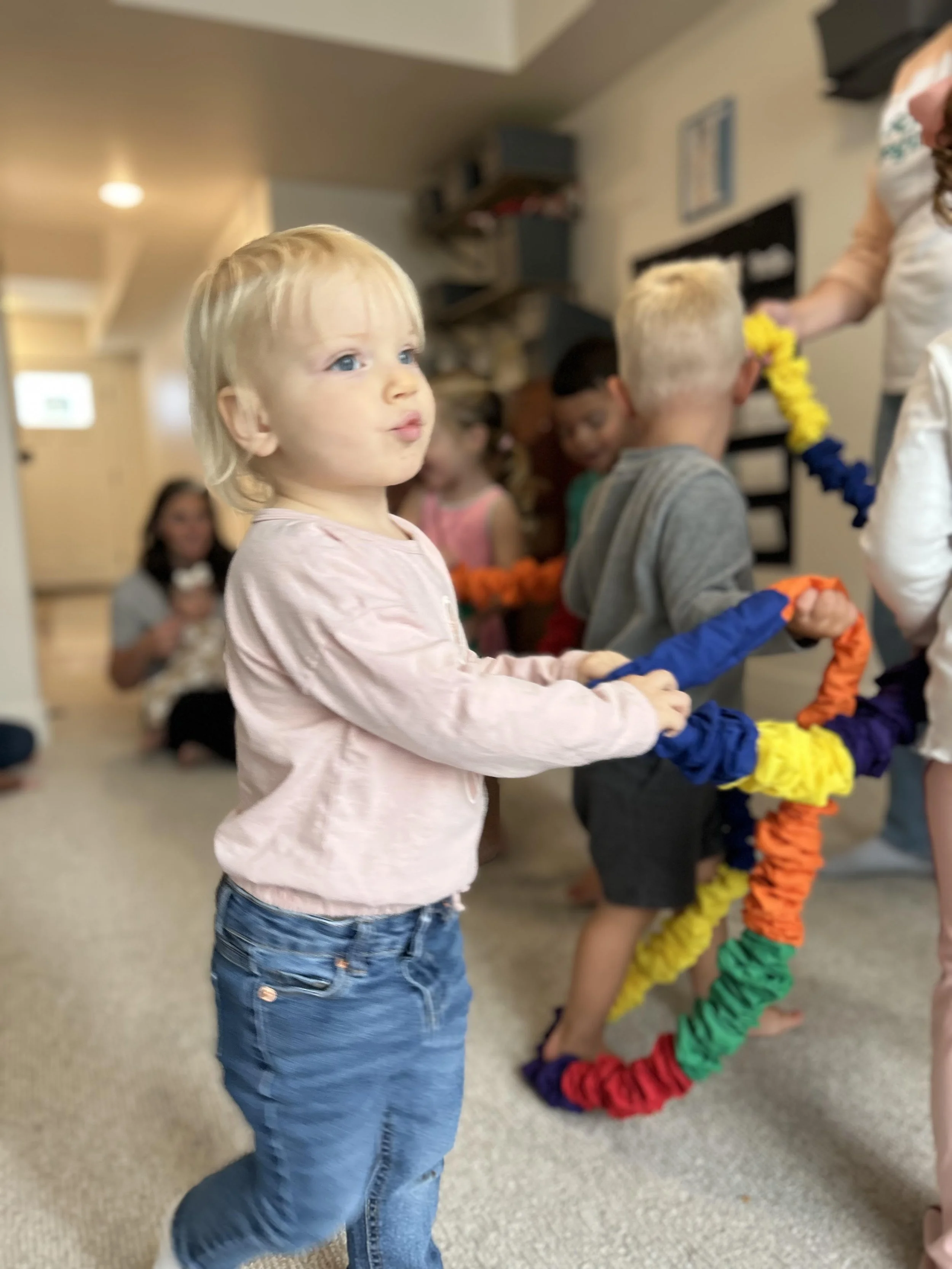 Young blonde girl in a pink shirt and jeans holding a colorful paper chain at a children's party.