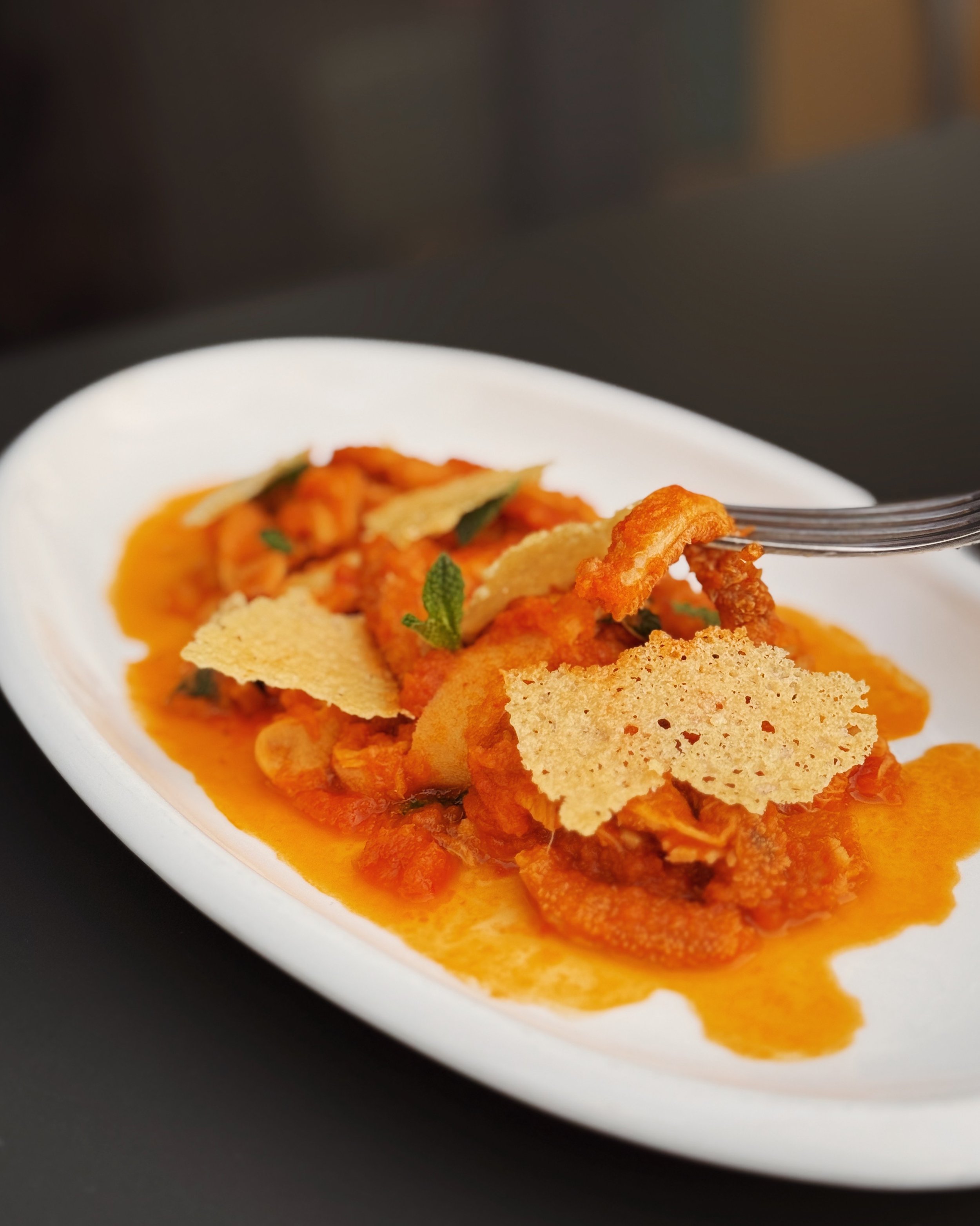 A white oval plate of Italian food with tomato sauce, crispy breaded fish, parmesan cheese, and fresh herbs.