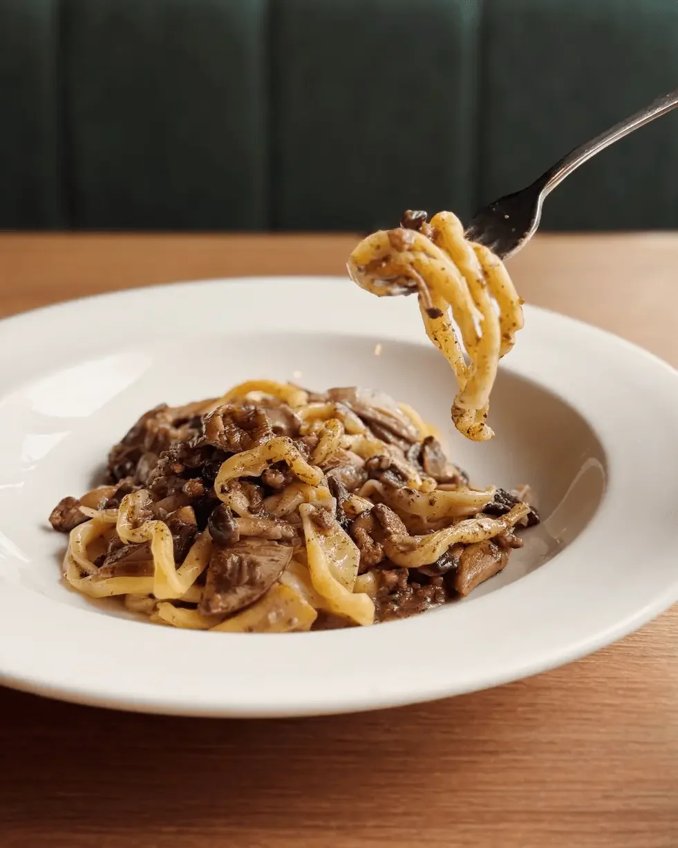 Plate of fettuccine pasta with mushrooms and sauce on a wooden table.