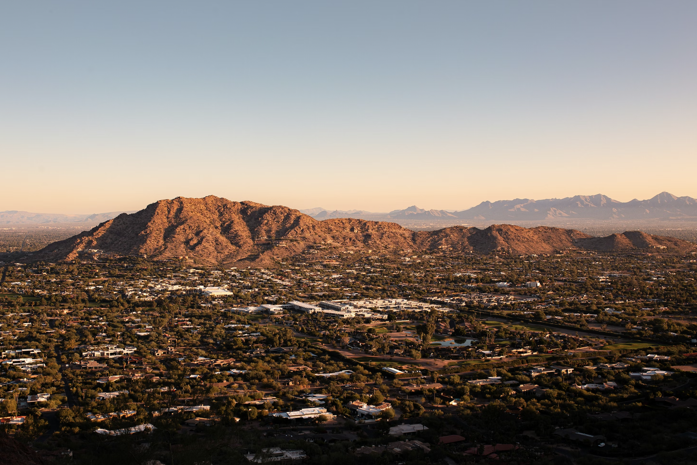Aerial view of a city with a mountainous landscape in the background during sunset.