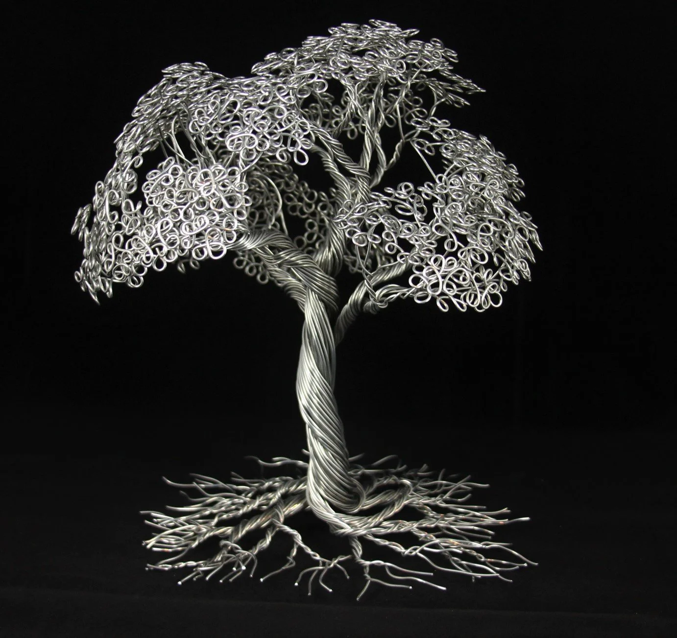 Silver wire sculpture of a tree with detailed roots, trunk, and leafy canopy, set against a black background.