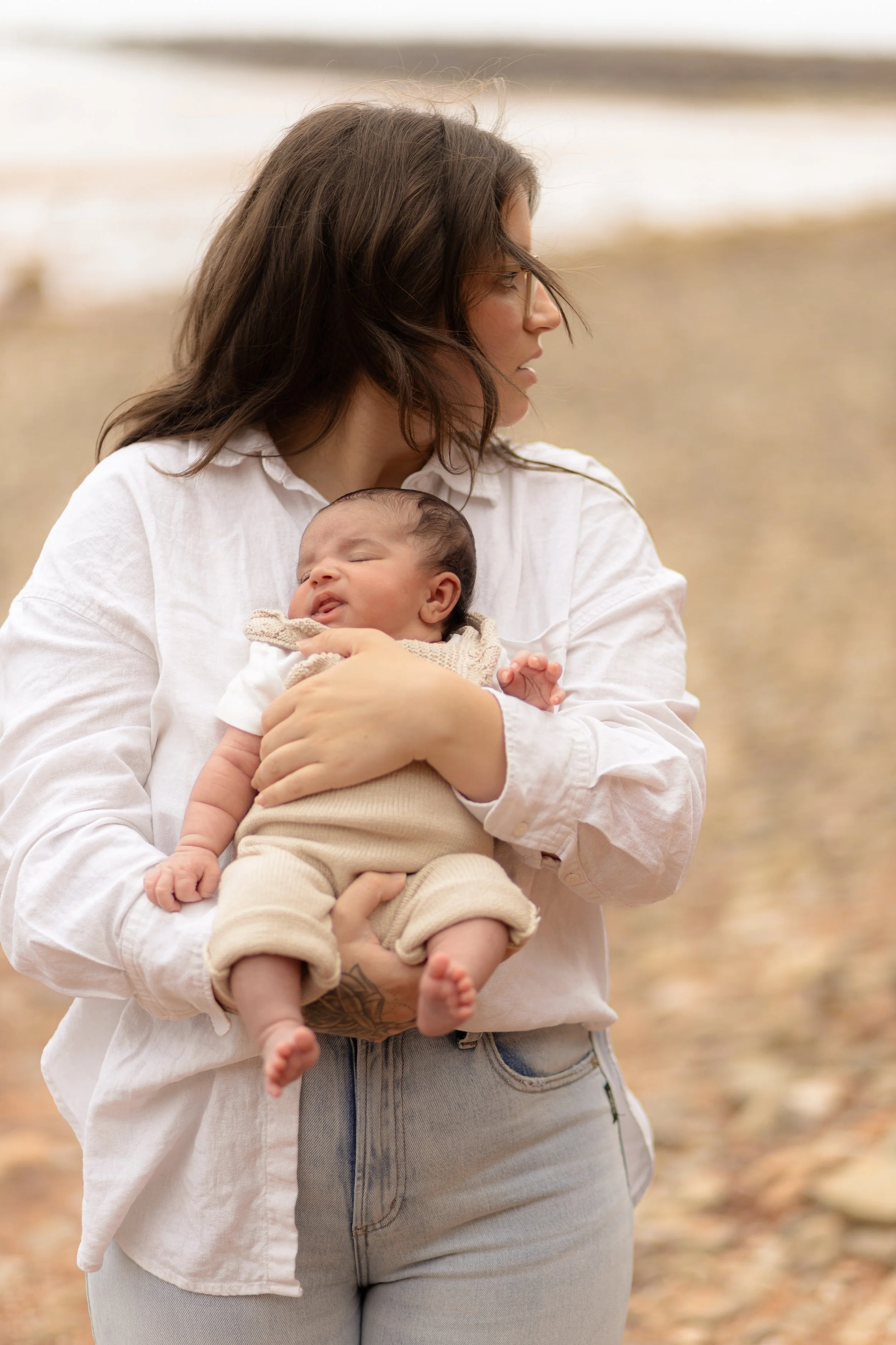 A woman holding a sleeping baby outdoors on a beach