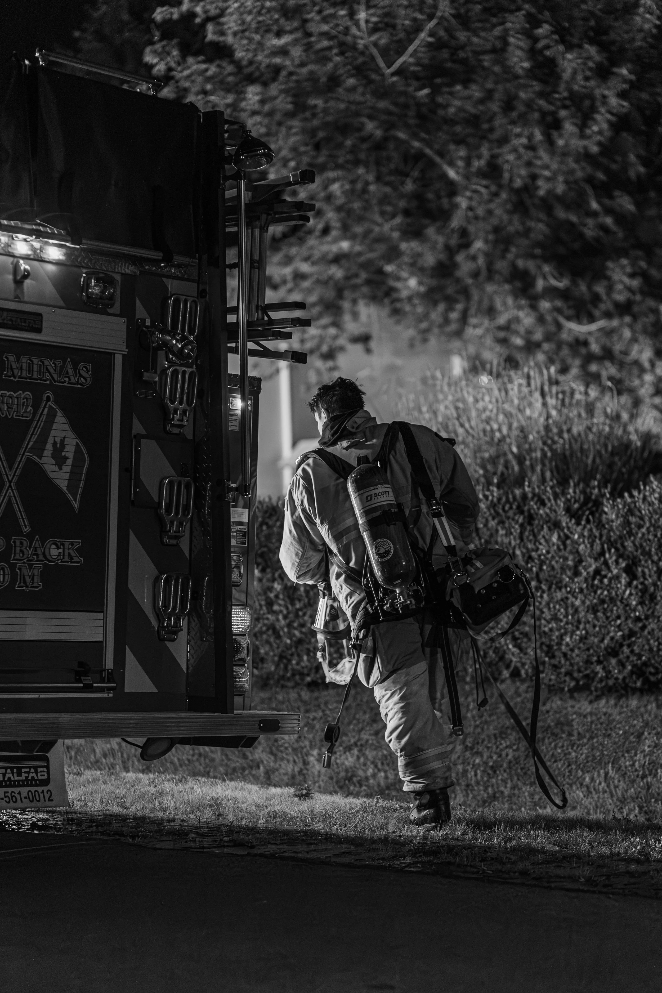 Firefighter walking away from a fire truck at night in a rural or suburban area.