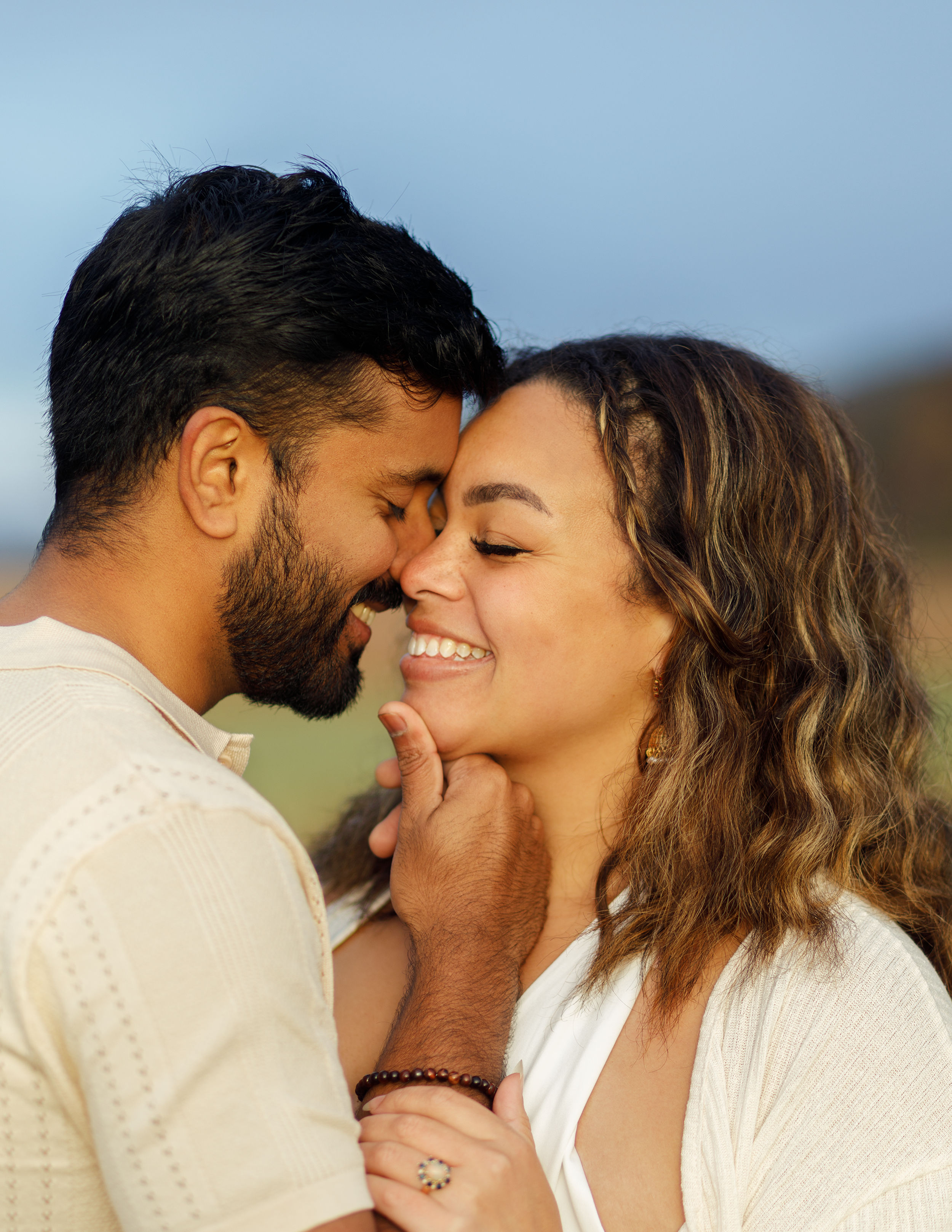 A happy couple with their faces close, smiling and touching noses outdoors.