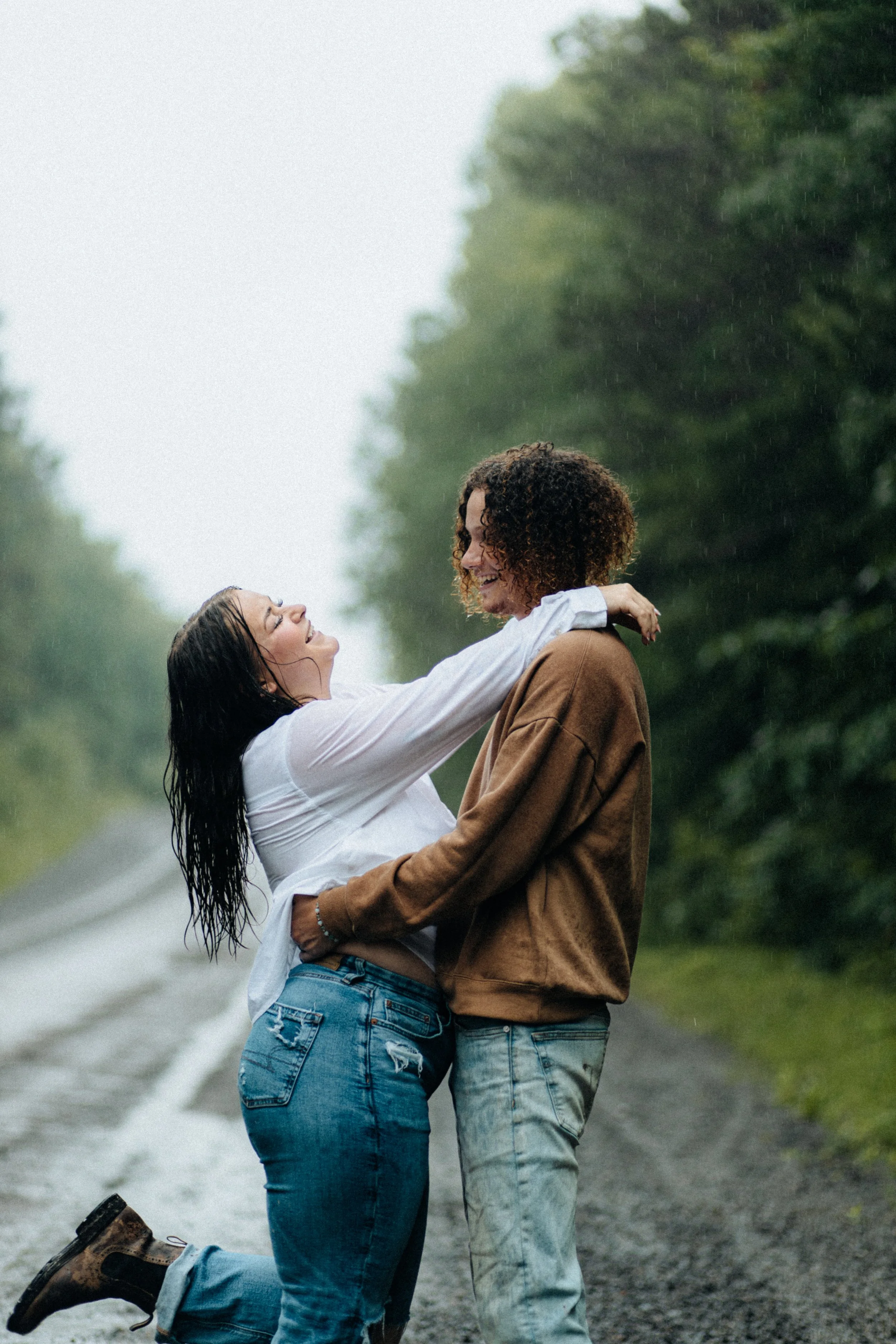 Two women embracing and smiling in the rain on a wooded road