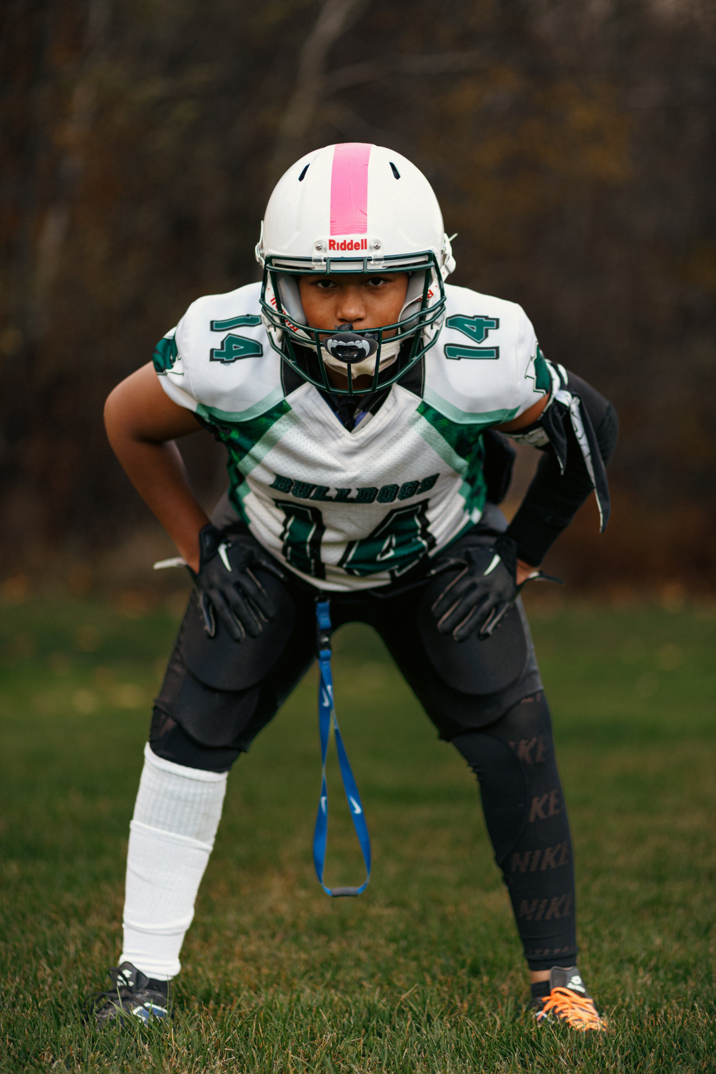Football player in a white helmet, black gloves, and black pants, crouching on a grassy field during daytime.