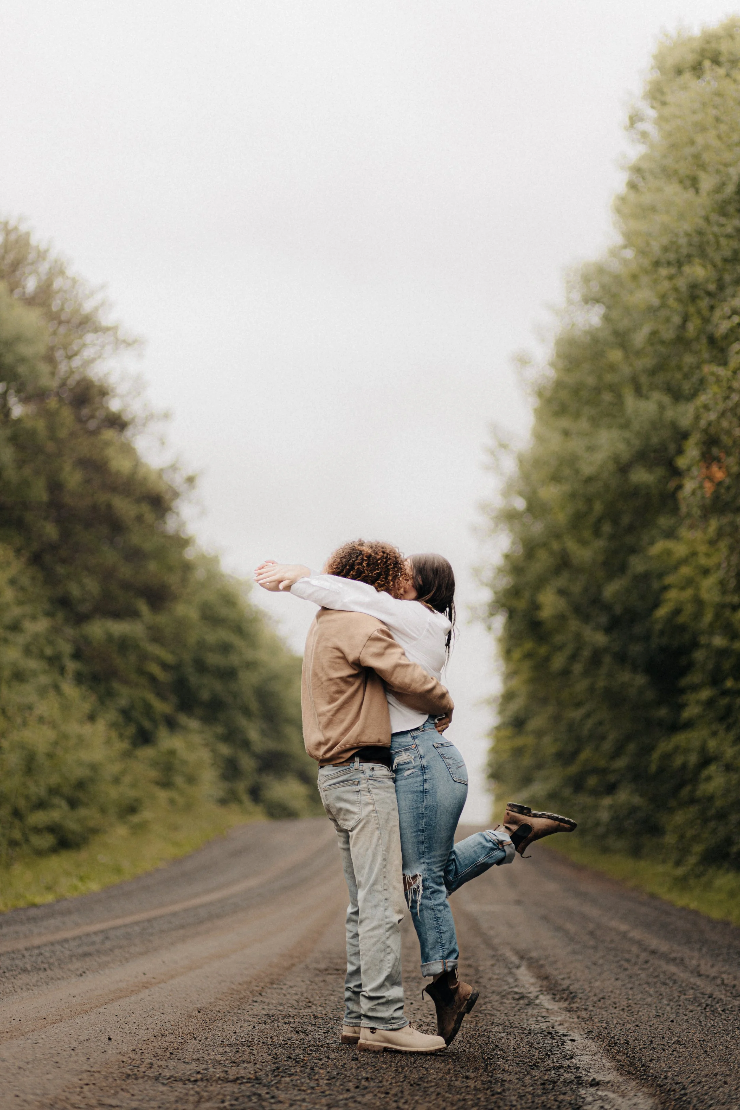 A couple hugging on a dirt road surrounded by green trees.