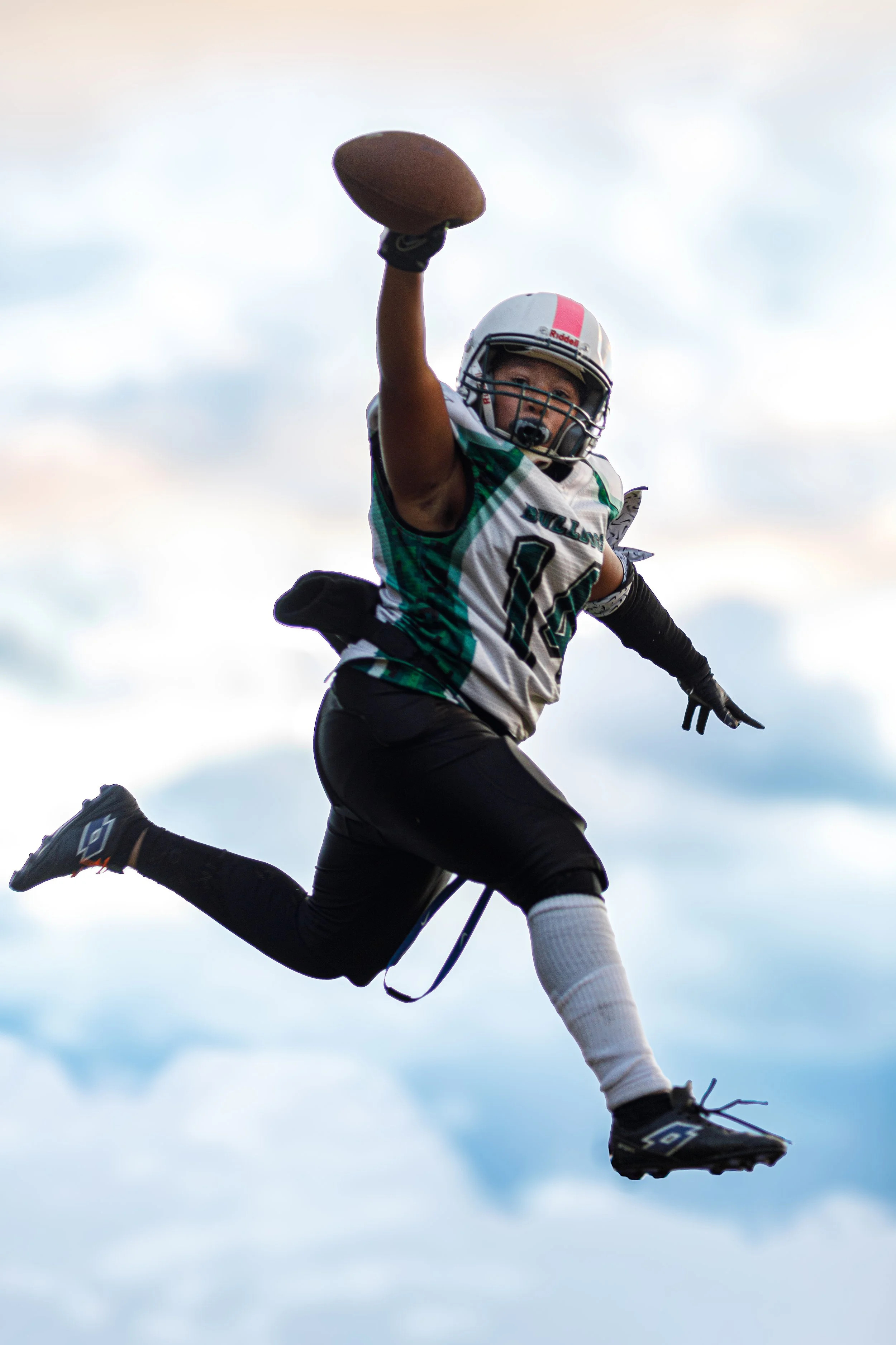A football player in mid-air catching a football against a cloudy sky.