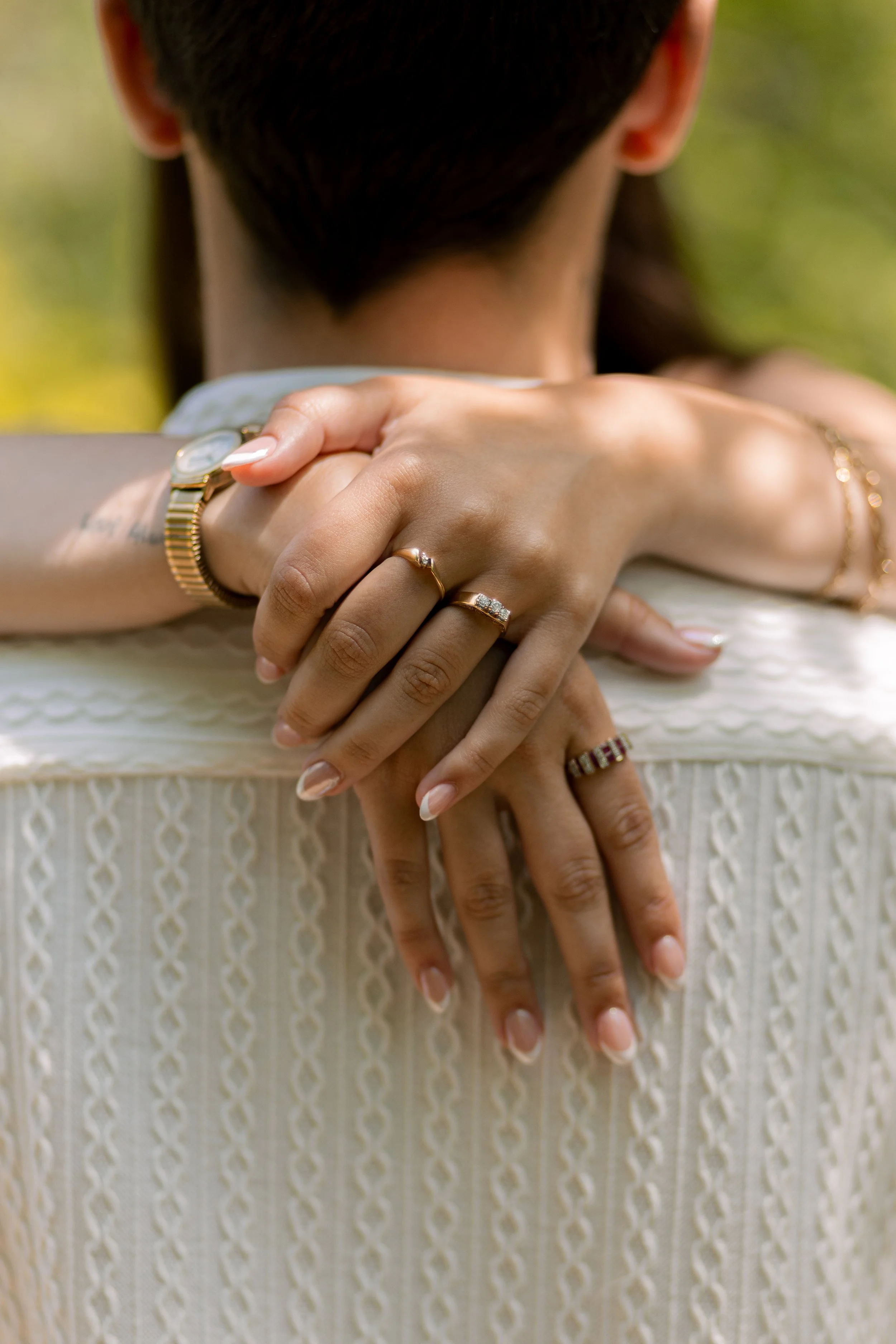 Woman's hands and arms showing jewelry resting on her shoulders, blurred green background.