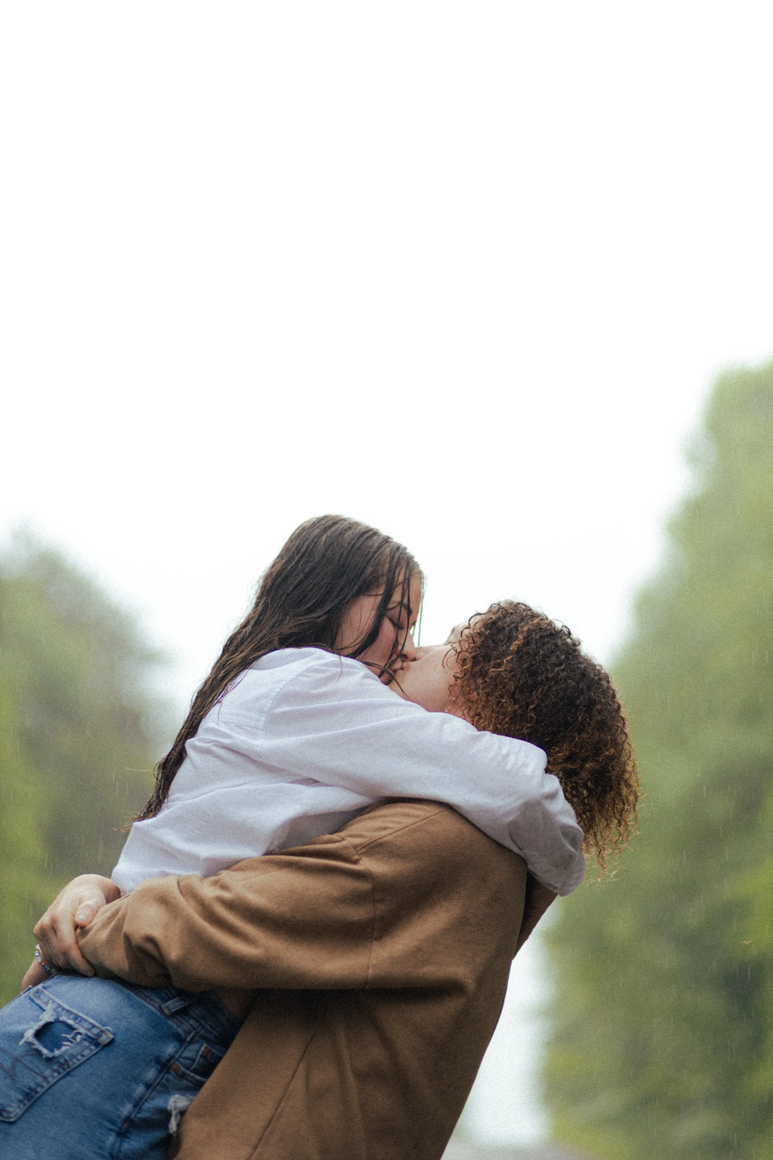 Two women sharing a kiss in the rain, outdoors, with a blurred green background.