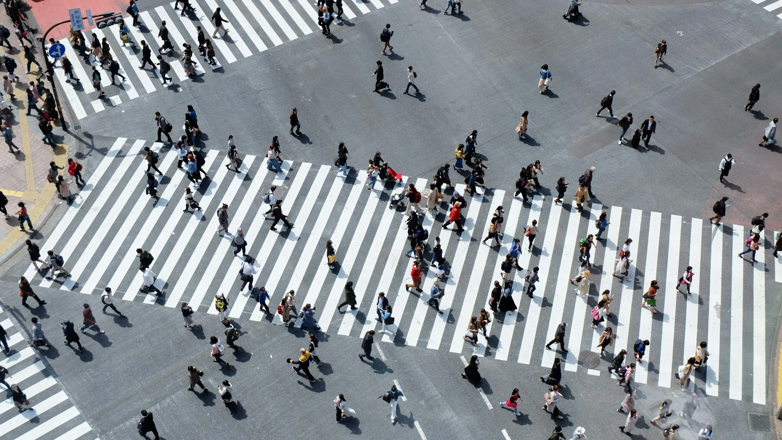 Bird's eye view of a busy city intersection with multiple crosswalks, filled with pedestrians walking in different directions.