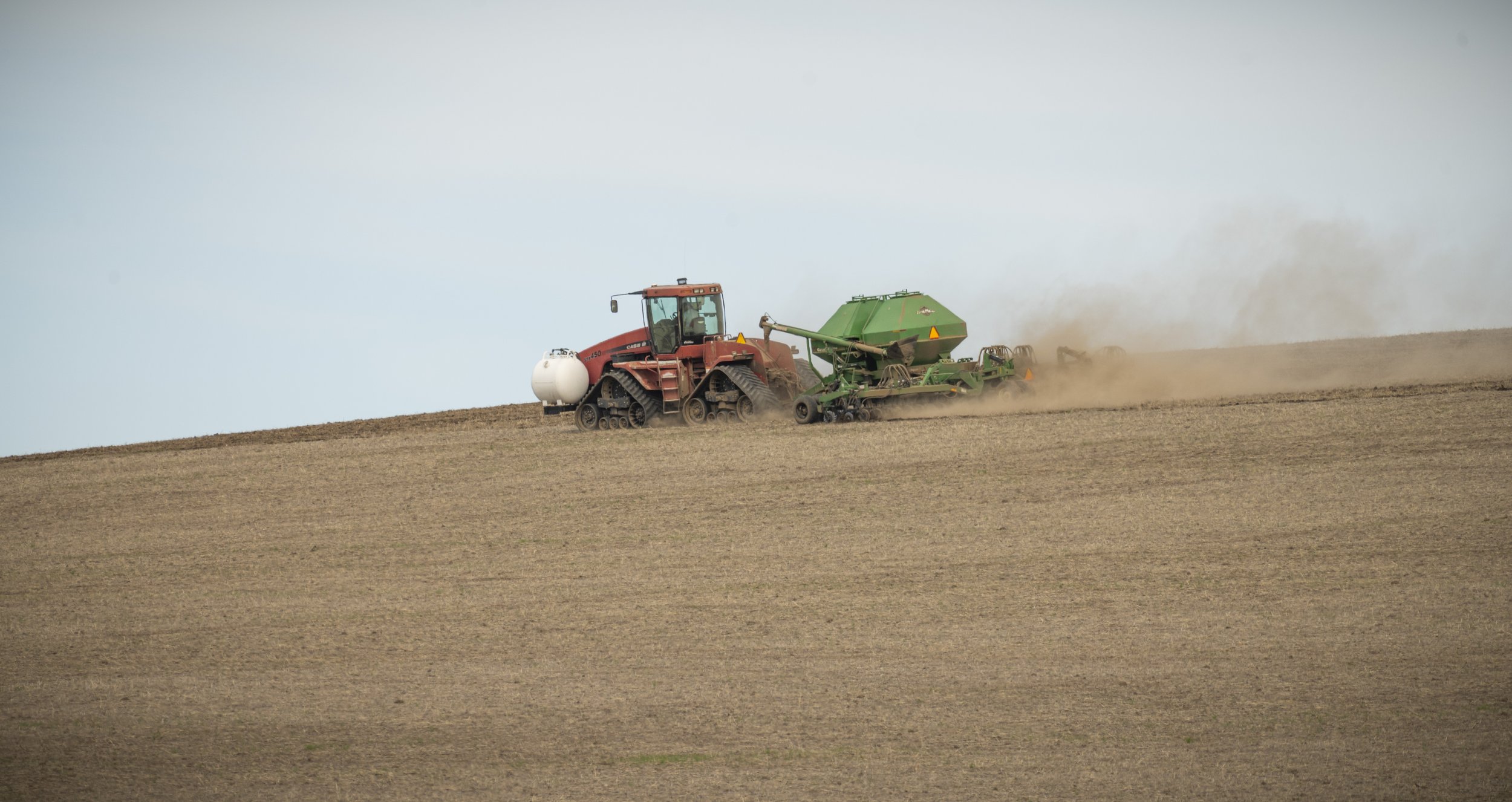 A tractor is planting wheat on a large field in the Walla Walla Valley, with dust in the air and a clear sky in the background.