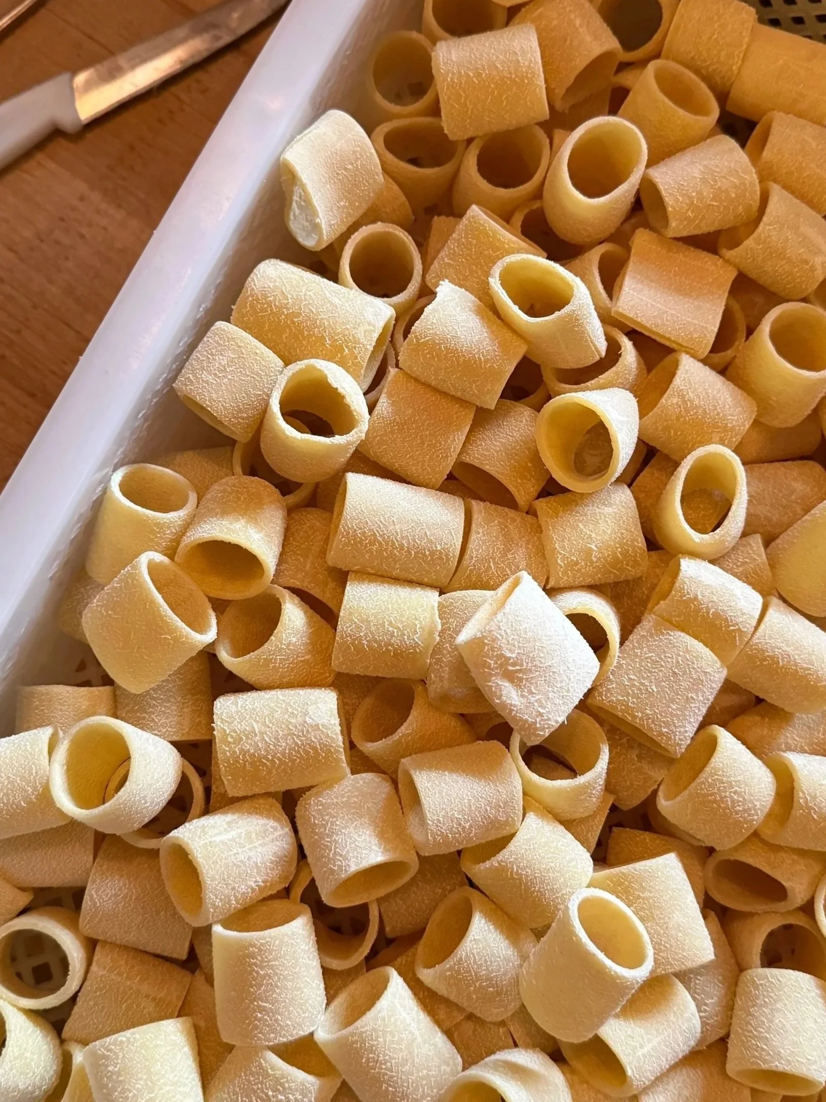 Close-up of uncooked pasta tubes with a floury surface resting on a wooden surface.