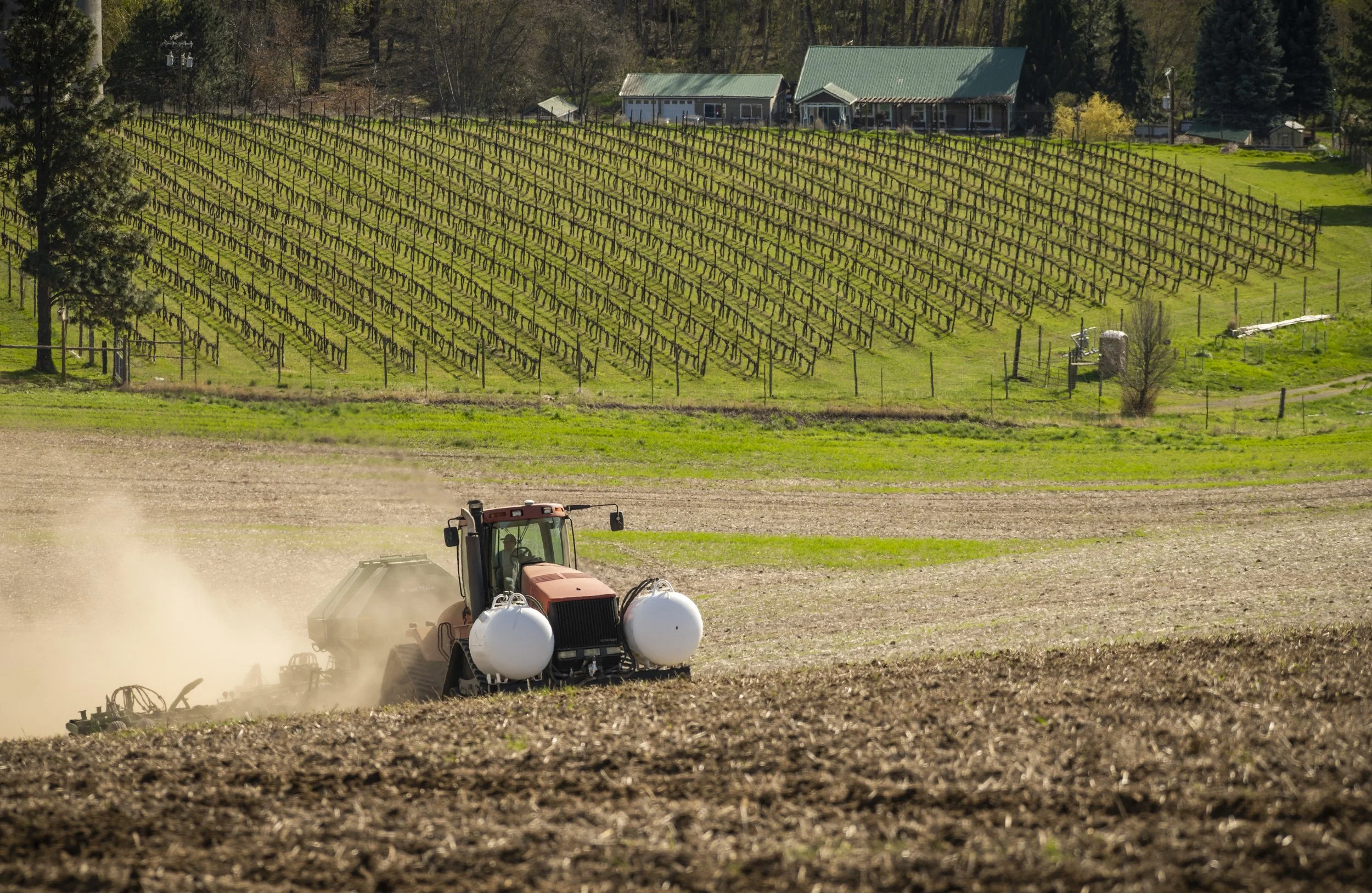 A tractor with large white sprayers working on a freshly plowed field.