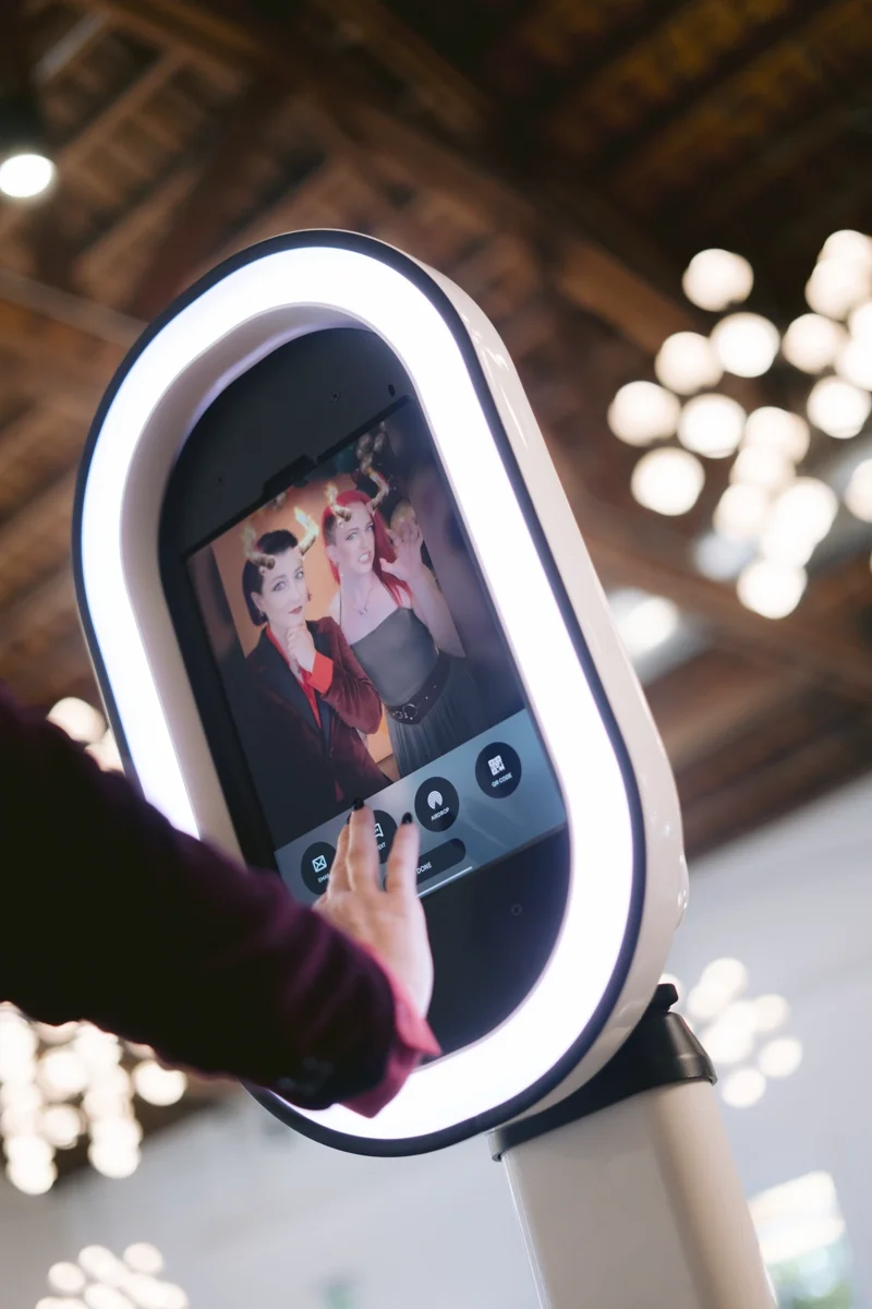 A person in a suit touching a touchscreen photo booth displaying a picture of a man and woman in formal attire.