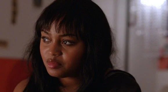 A woman with dark hair and bangs looking to her left in an indoor setting.