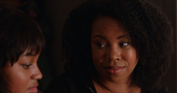 Two women in a dimly lit setting, engaged in conversation, with one looking at the other.