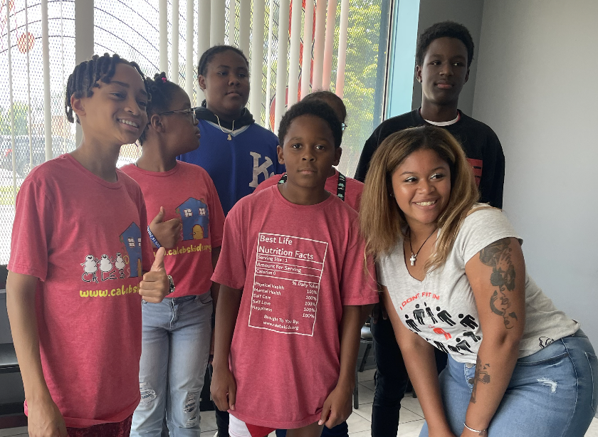 Group of six diverse children and a young woman posing indoors, some smiling and looking at the camera.