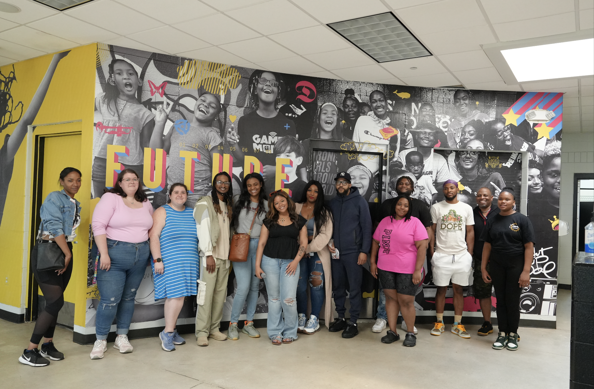 Group of diverse people standing in front of a modern wall mural with black and white photos of children and the word 'FUTURE' in large colorful letters.