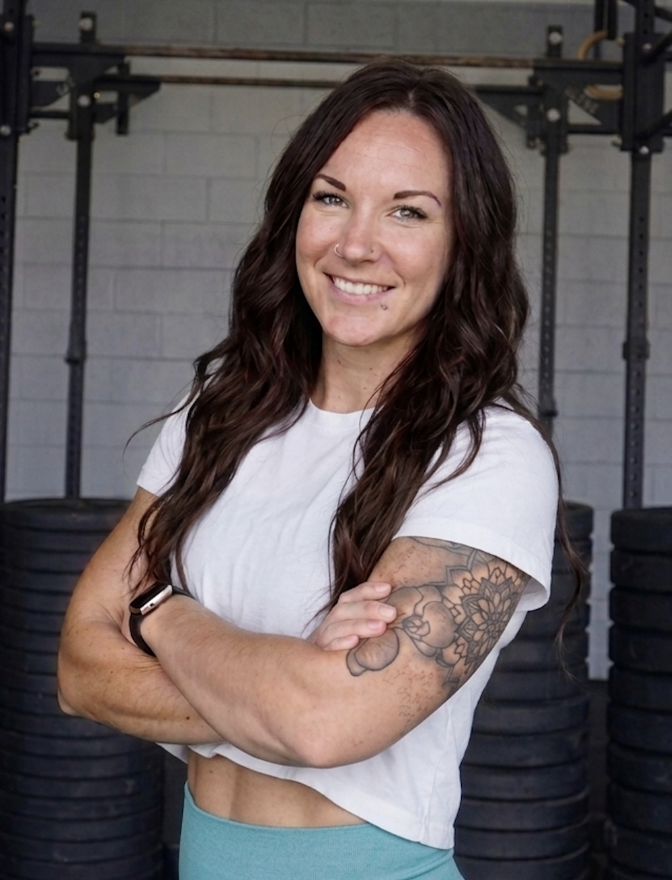 Amber, smiling, standing with her arms crossed inside the gym