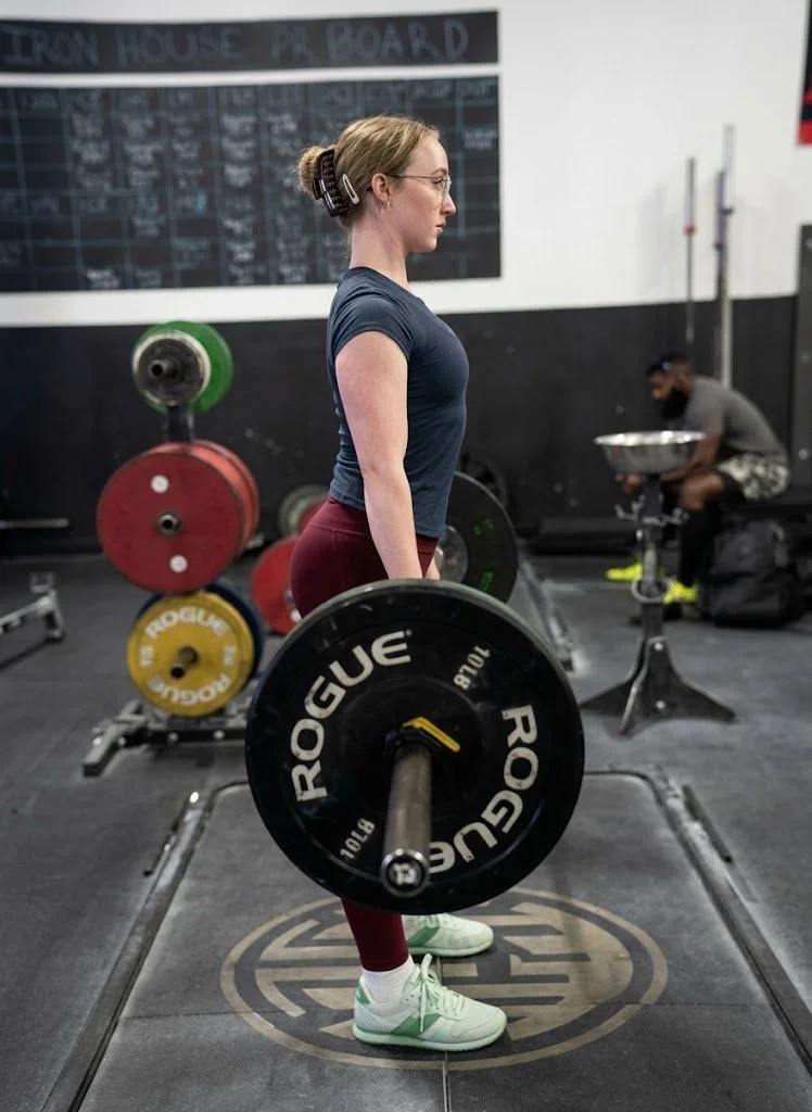 A client standing tall with a loaded barbell at Iron House Gym