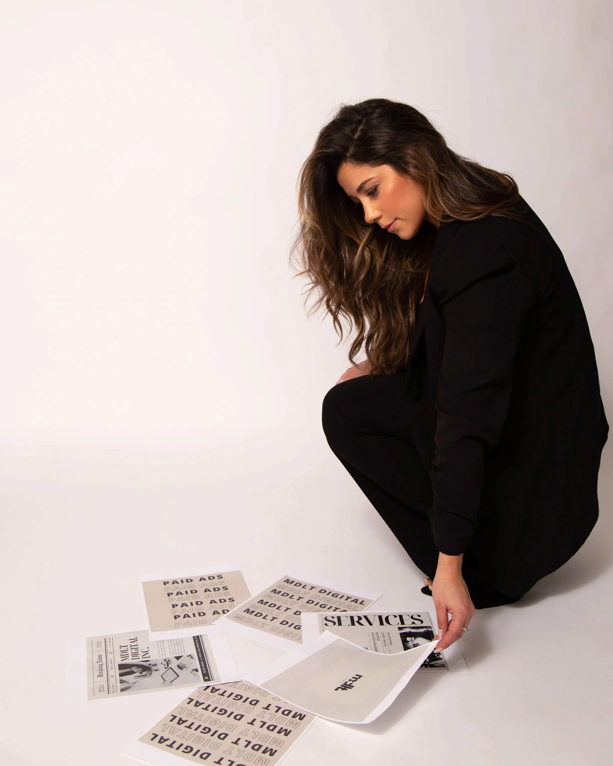 Woman crouching down in black clothing, sorting through printed sheets and flyers on the floor.