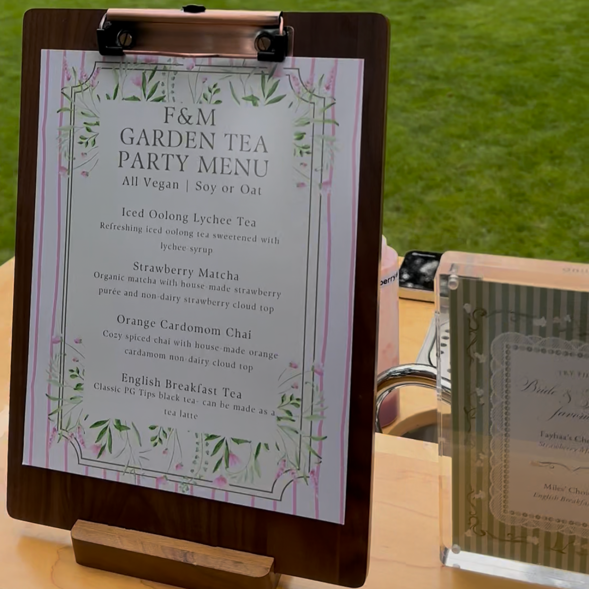 Menu sign for F&M Garden Tea Party, offering vegan options with soy or oat milk. Includes iced oolong lychee tea with lychee syrup, strawberry matcha with house-made strawberry purée, orange cardamom chai, and English breakfast tea.