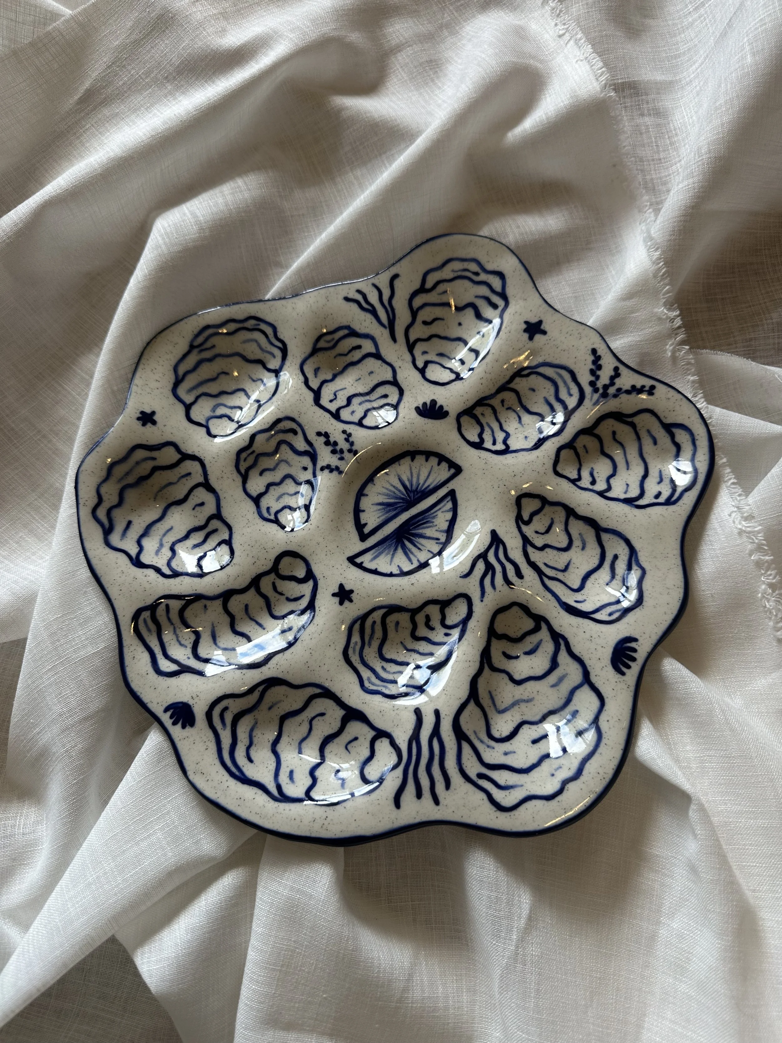 A decorative ceramic plate with blue floral and abstract patterns on a white background, placed on a light-colored fabric surface.