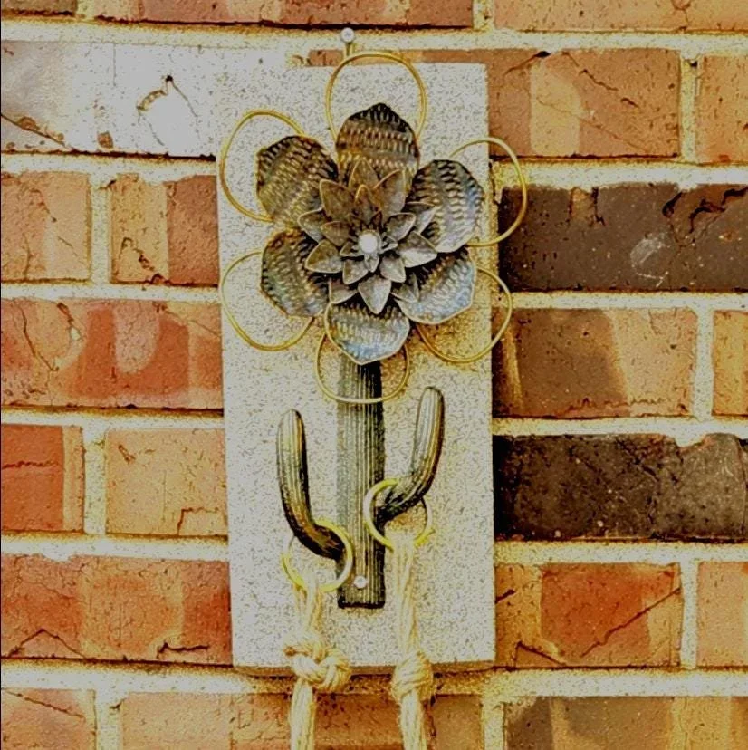Decorative metal cactus and flower wall hanging mounted on a brick wall.