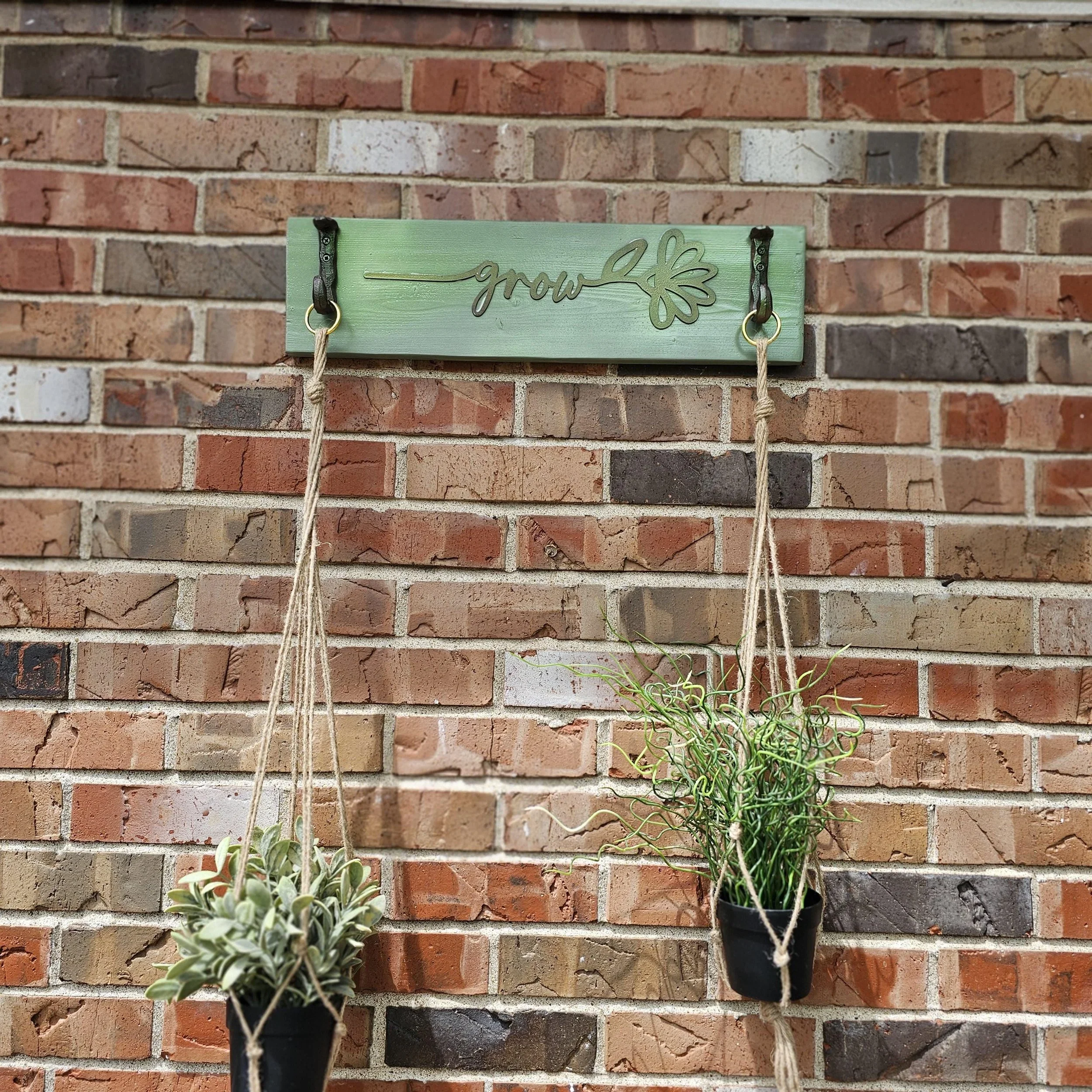Brick wall with a green decorative sign that says 'grow' and two hanging planters with plants.