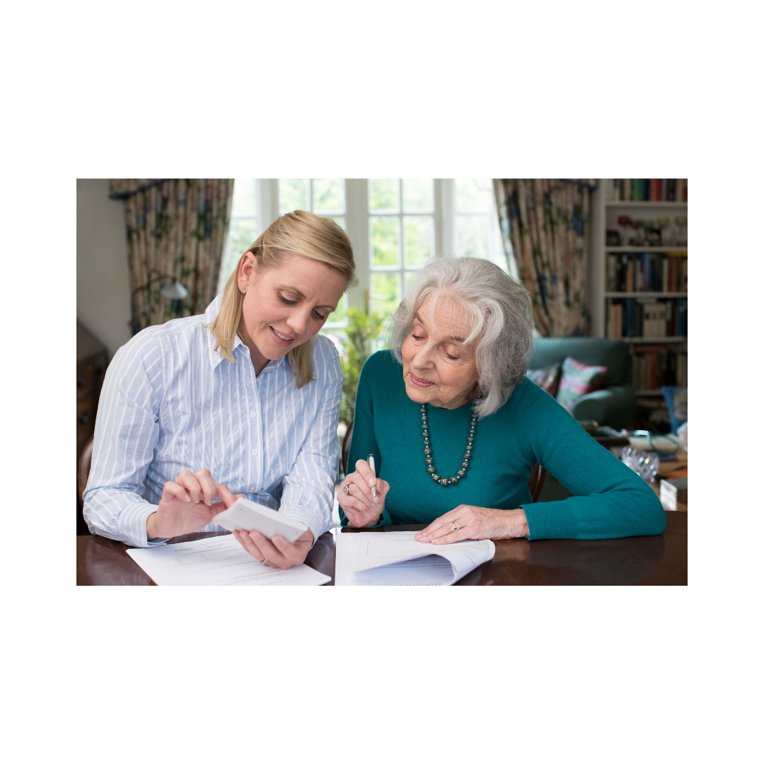 Two women, one elderly with white hair and one younger, sitting at a table, looking at documents and discussing financial matters in a cozy, well-lit room.