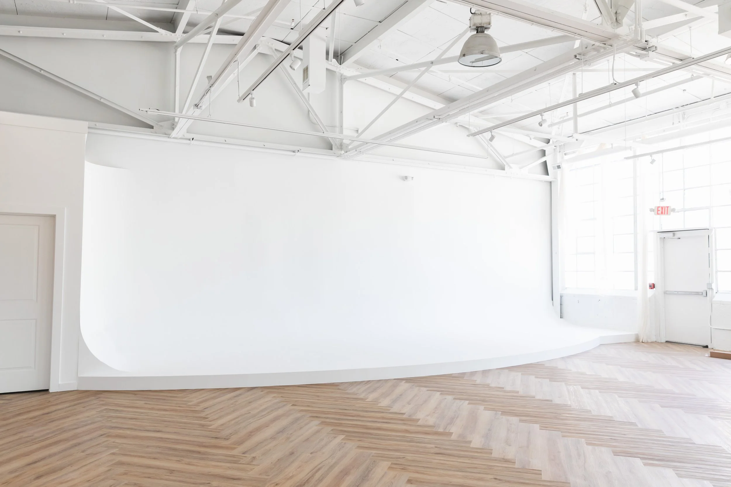 Empty photography studio with white backdrop, high ceiling, and wooden floor.