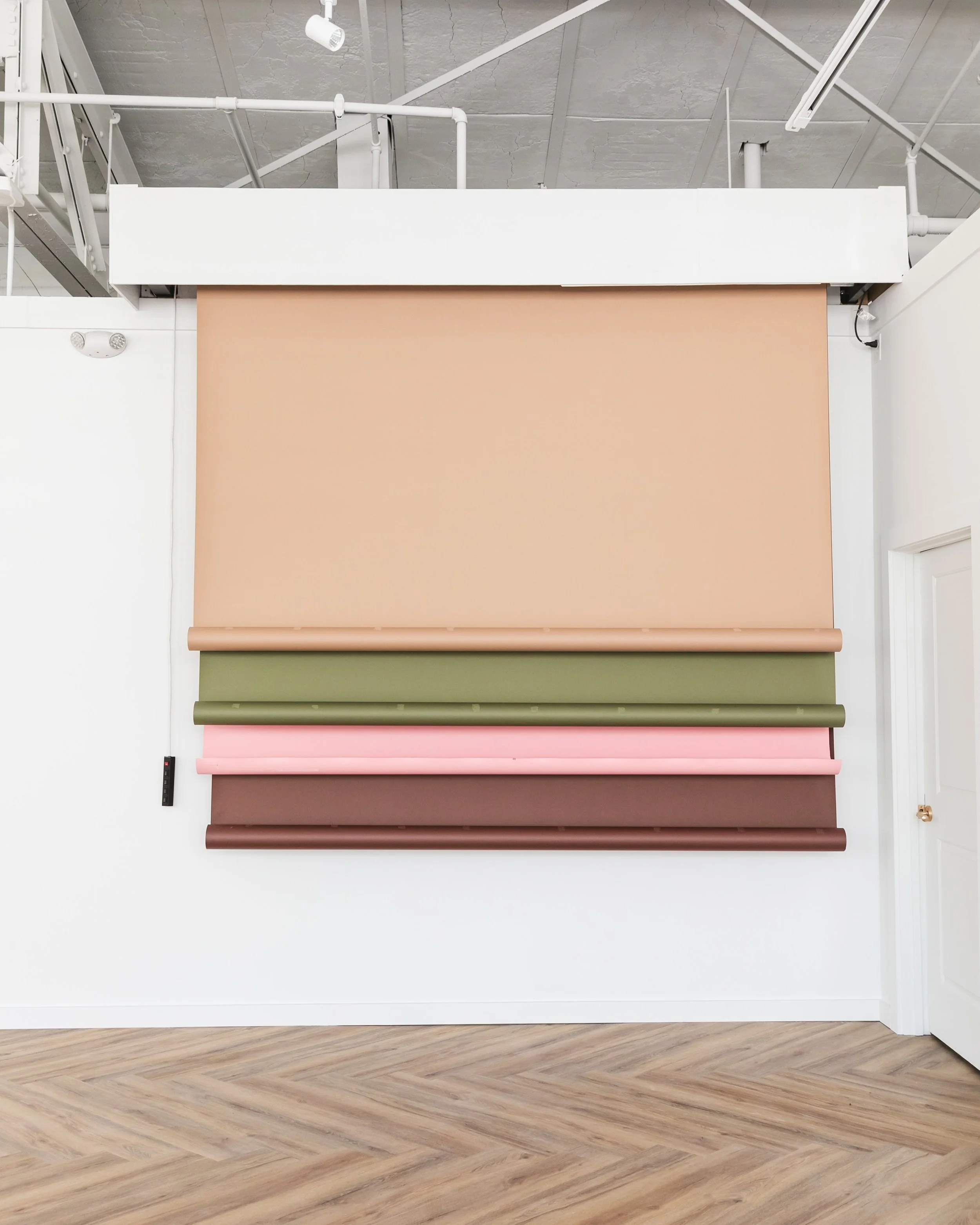Display of various rolled-up window blinds in neutral and pastel colors on a white wall in a showroom.