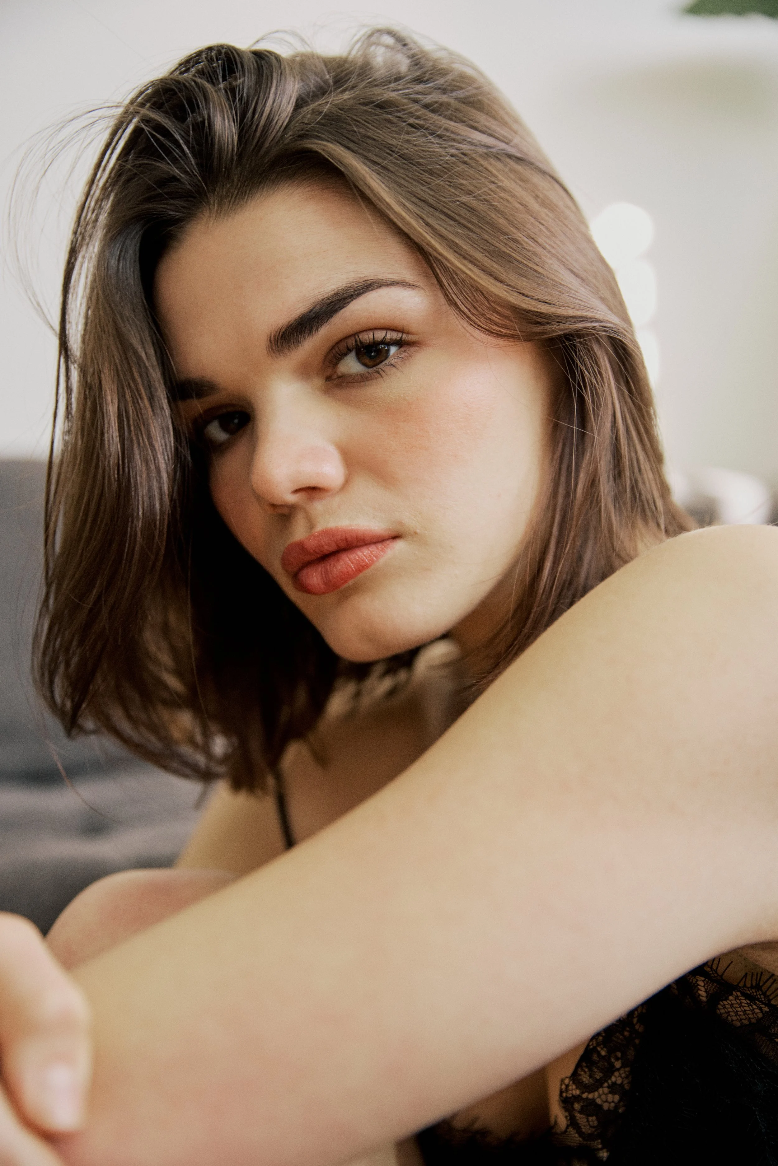 Close-up of a woman with brown hair, looking at the camera with a slightly serious expression, wearing black lace clothing.