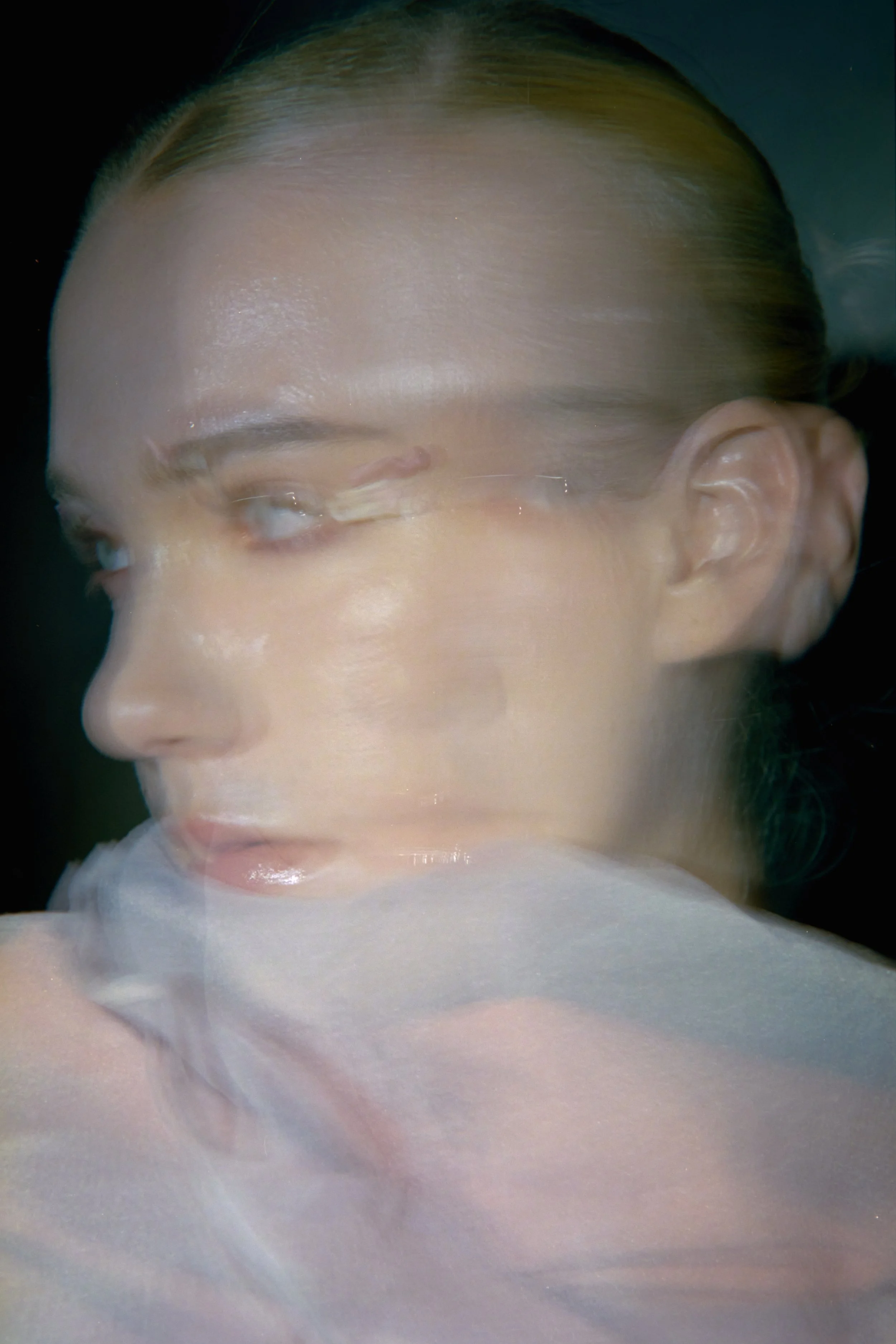 Close-up of a person's face with makeup, lying on a surface, with light reflecting on their skin and hair pulled back.