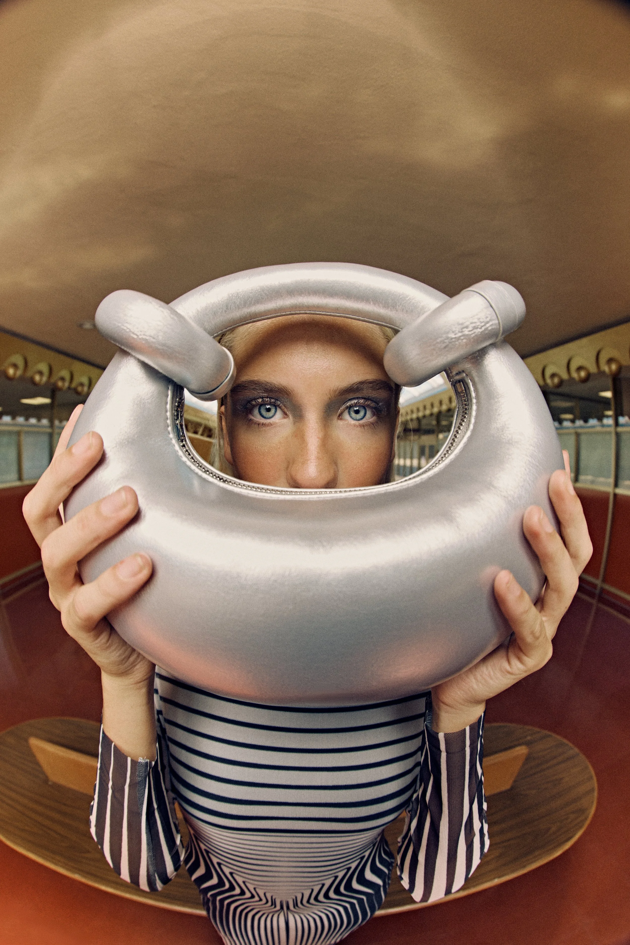 Person holding a metallic kettlebell in front of their face, with bright blue eyes visible through the handle.