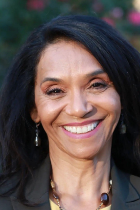 A woman with black hair smiling, wearing earrings and a blazer.