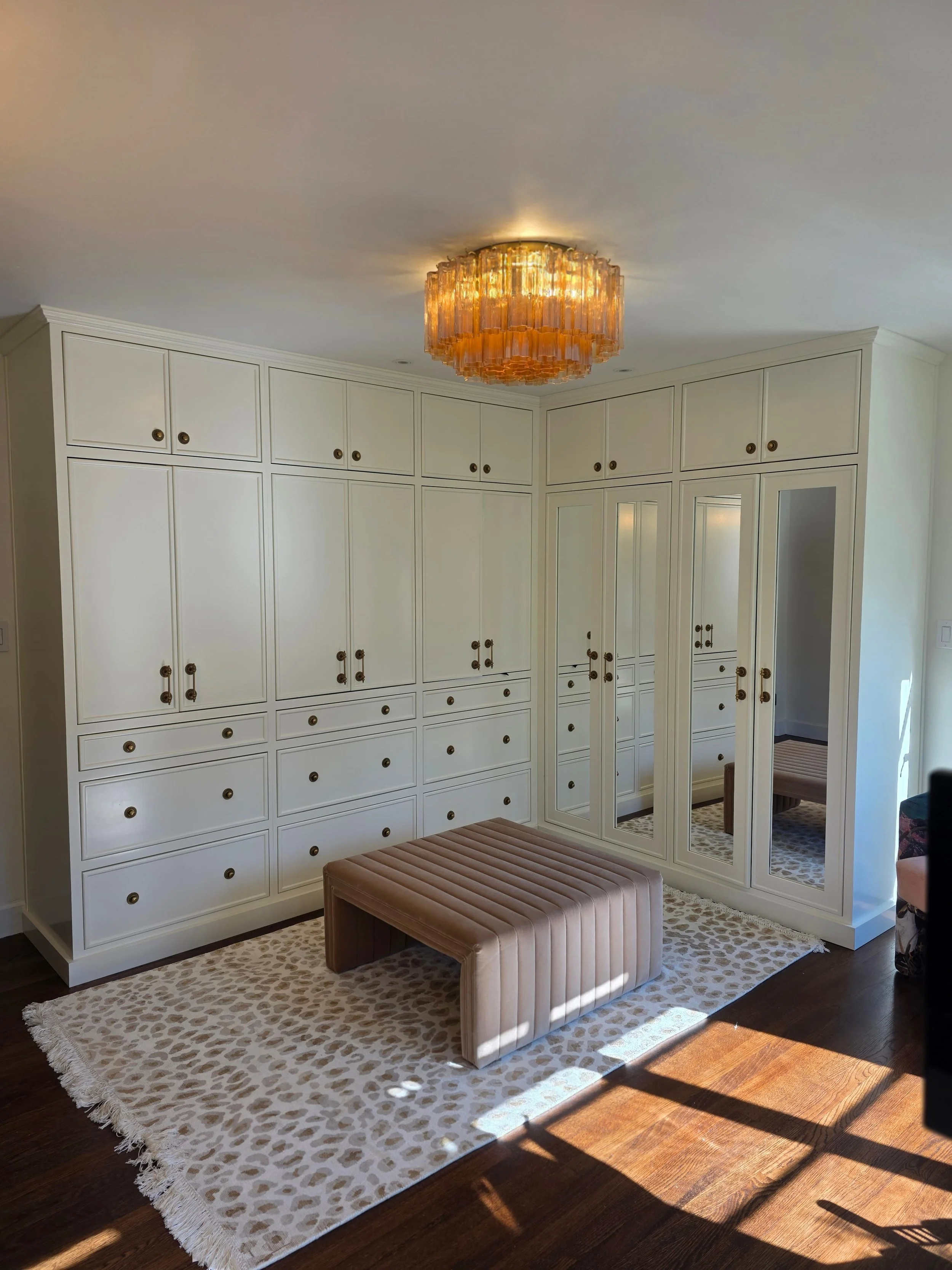Luxury large walk in closet. Vintage white cabinets with gold accents. Mirror, lighting, and seating.