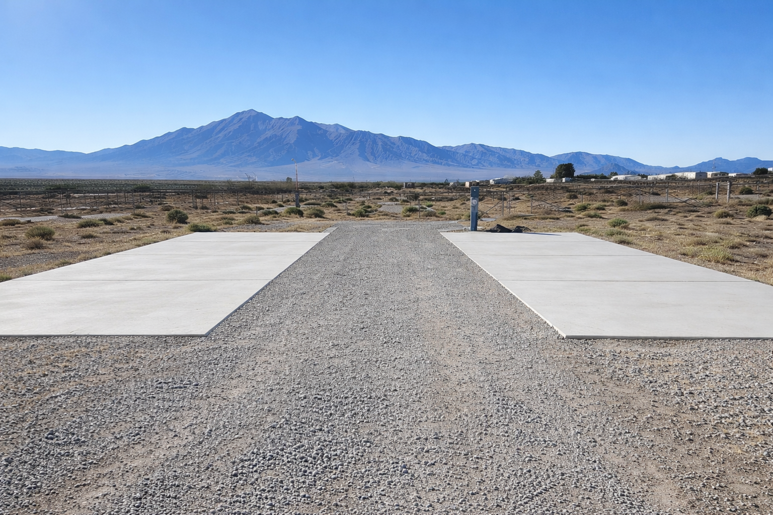 Empty parking space with concrete pads and a gravel pathway in front of a mountain landscape under a clear blue sky.