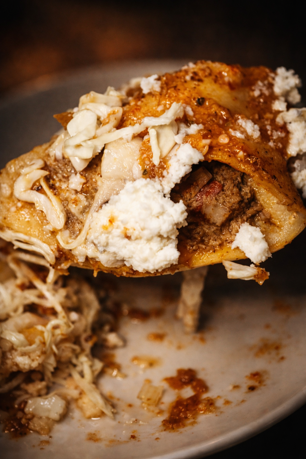 Close-up of a spoonful of a meat and cheese casserole with pasta, topped with shredded cheese, sour cream, and sauce.
