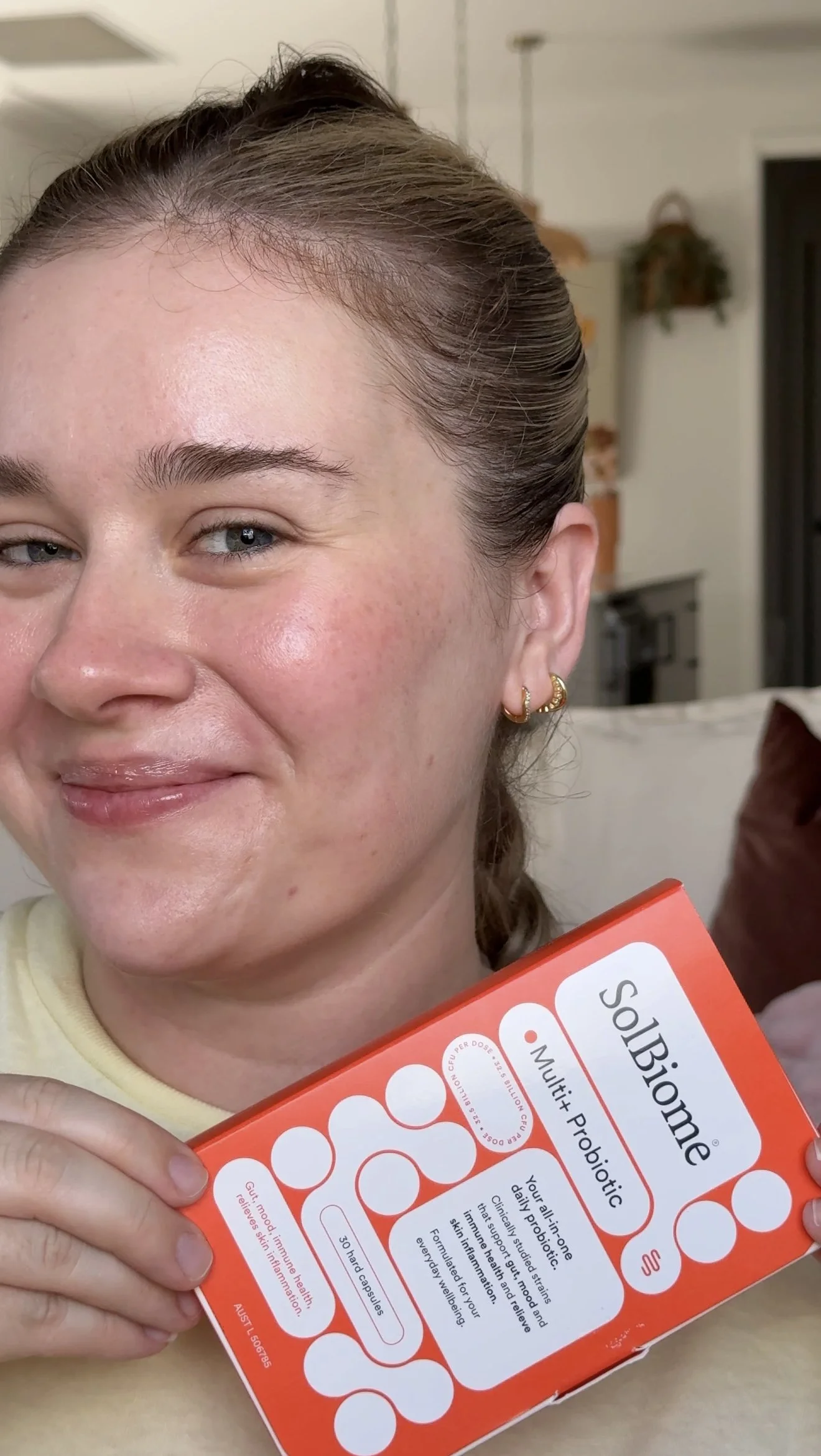 A woman smiling and holding a box of Biologique Multi Probiotic capsules in her hand.