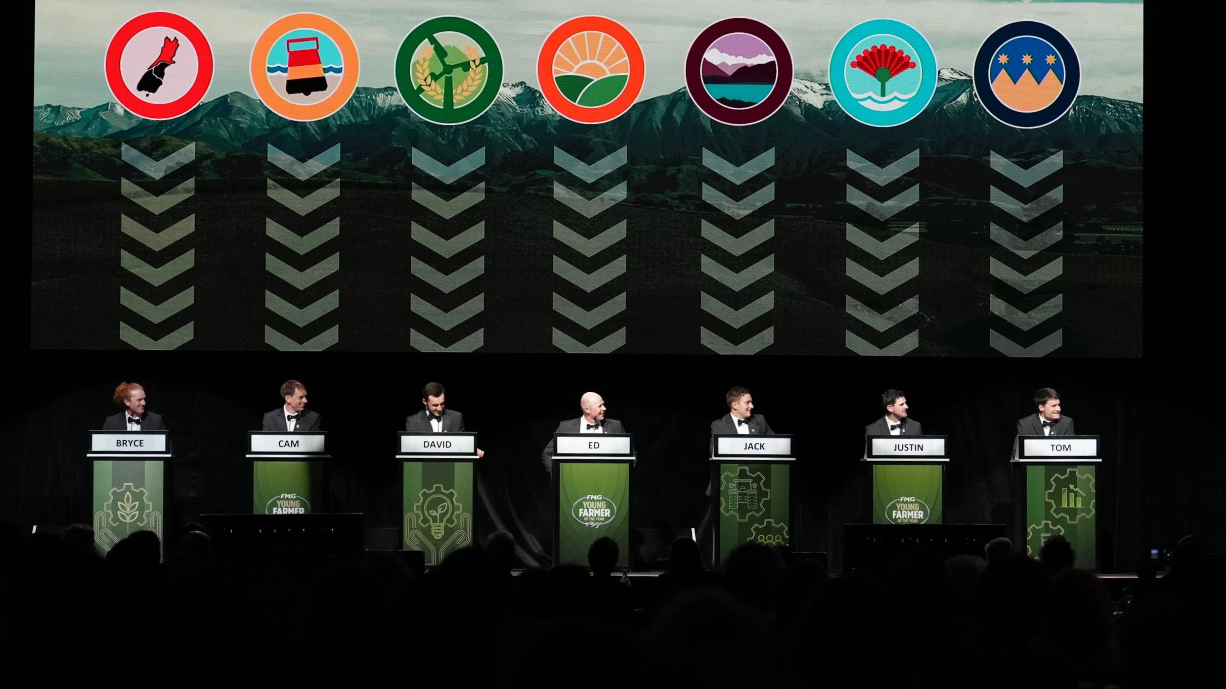 Six men in tuxedos standing at podiums on a stage, with a large screen behind them displaying icons of various agricultural and environmental symbols and the names Bryce, Cam, David, Ed, Jack, Justin, and Tom.