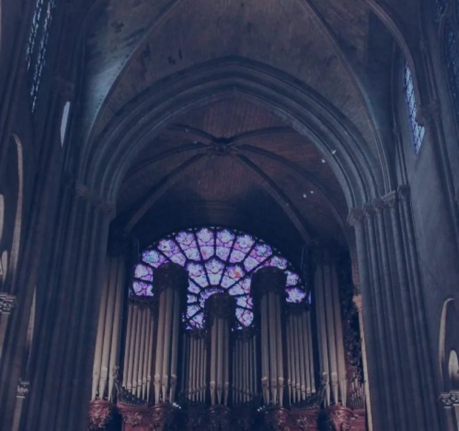 Interior view of a cathedral with stained glass window and large pipe organ.