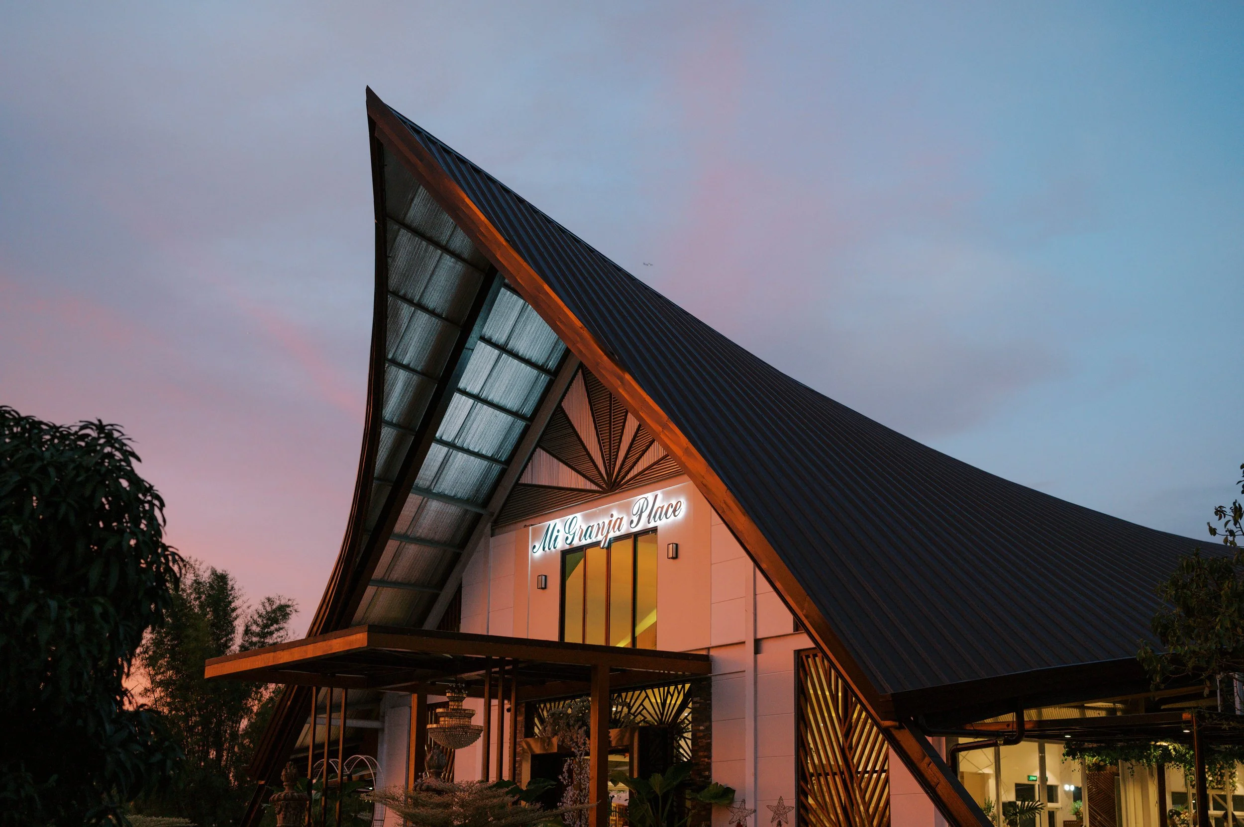 View of an architecturally unique building with a steeply sloped roof set against a colorful evening sky.
