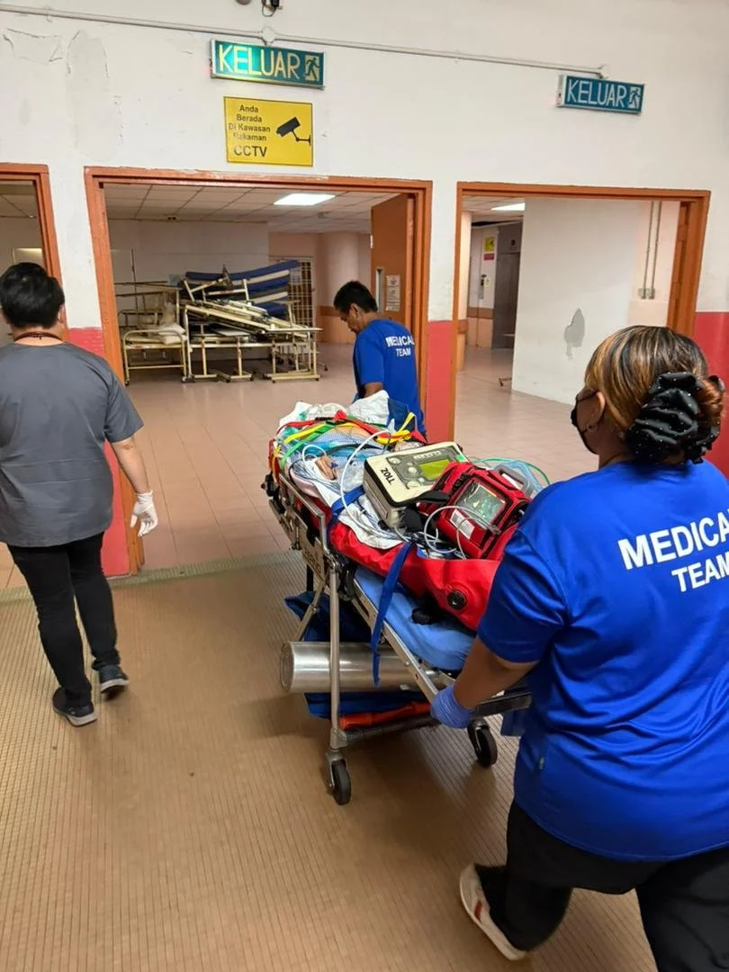 Hospital corridor with medical team pushing a stretcher loaded with medical equipment and supplies, likely in an emergency room setting.