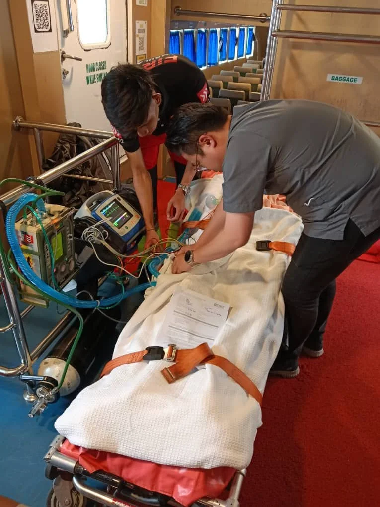 Medical personnel attending to a patient on a stretcher with medical equipment on a ship or hospital setting.