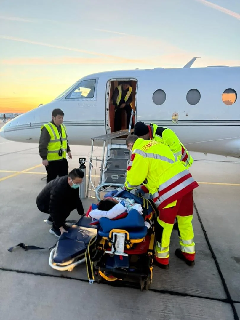 Emergency medical team attending to a patient on a stretcher outside an airplane on the tarmac during sunset.