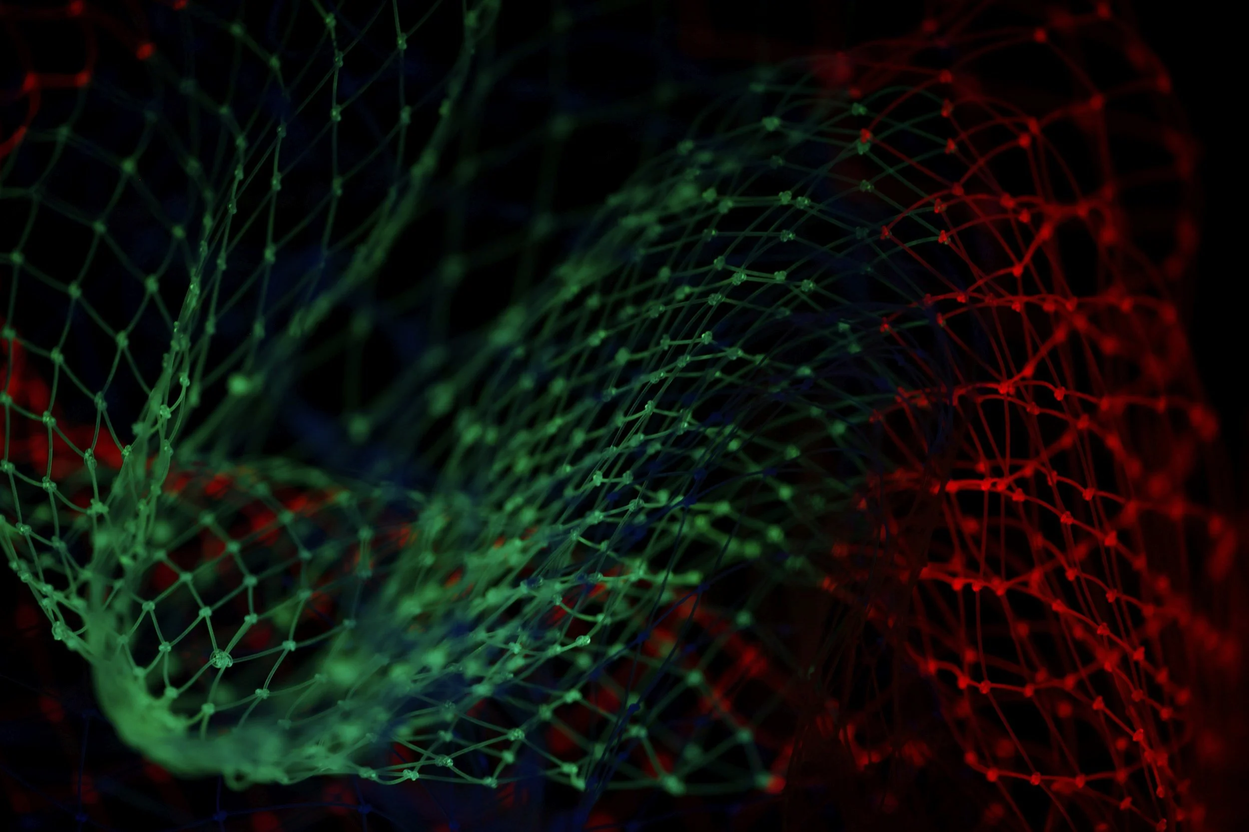 Colorful glowing web of interconnected lines and nodes in red and green against a black background.