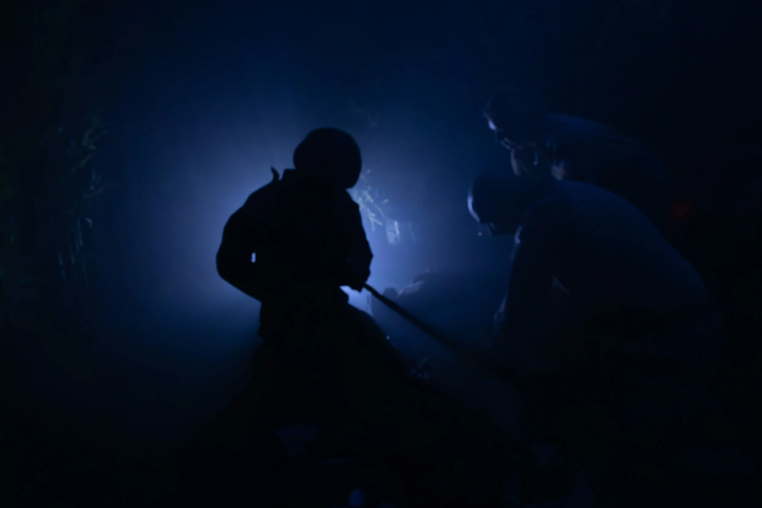 Silhouettes of two people in a dark environment with a bright light behind them.